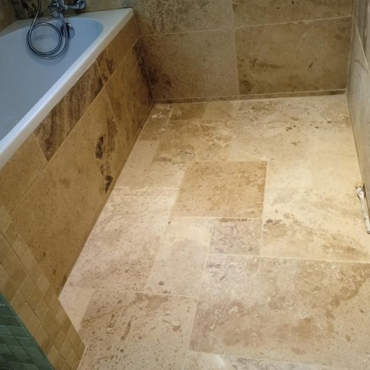 Salle de bains avec baignoire sur la gauche et carrelage en grès beige.