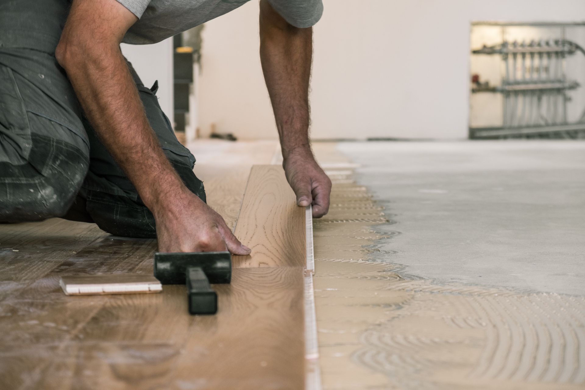 Un ouvrier lisse le sol en béton avec une truelle lors de la pose d'un parquet.
