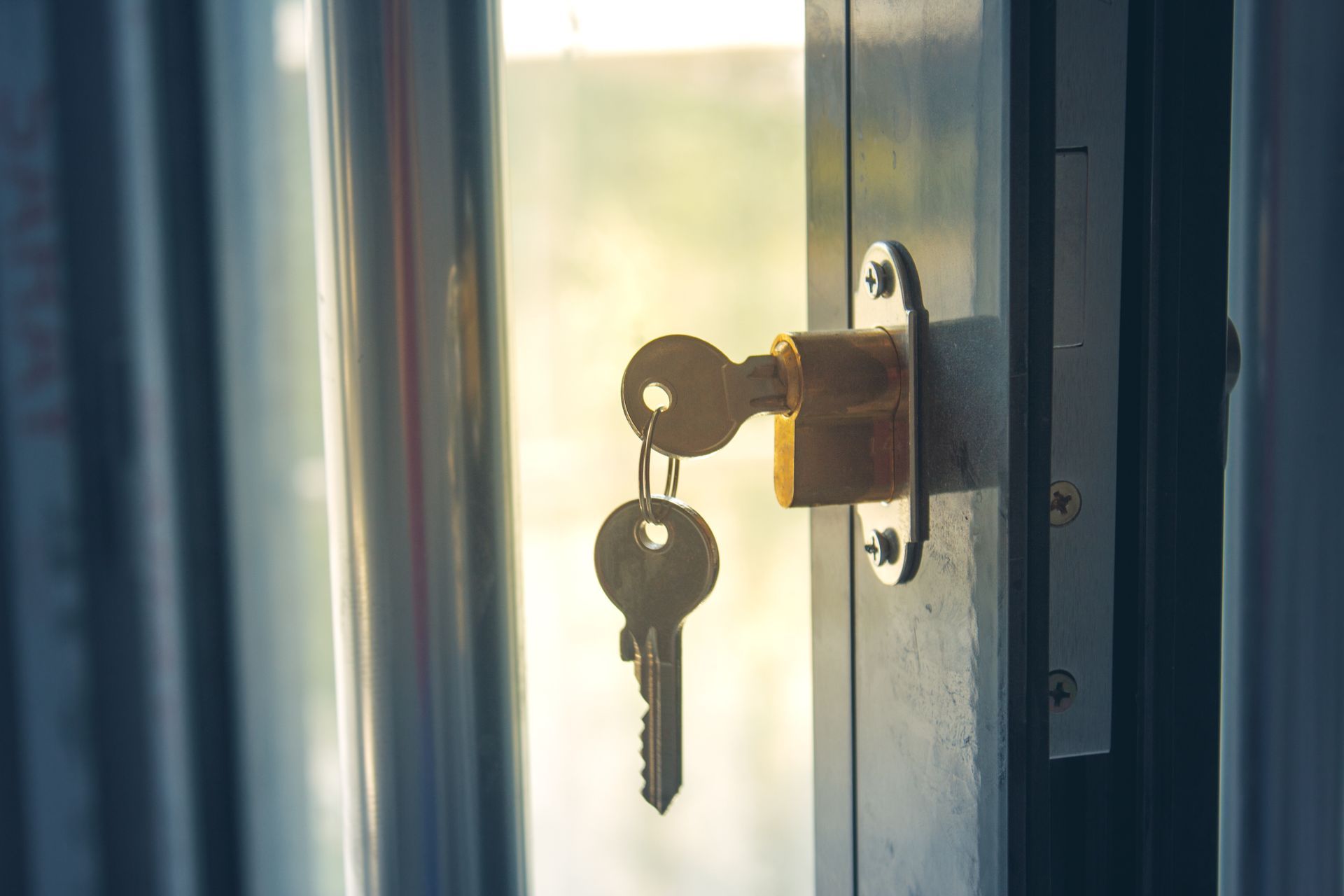 Clé dans une serrure sur une porte vitrée, éclairée par la lumière du soleil.