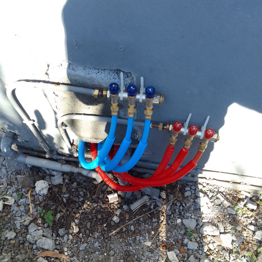 Installation de plomberie extérieure avec tuyaux bleus et rouges connectés.