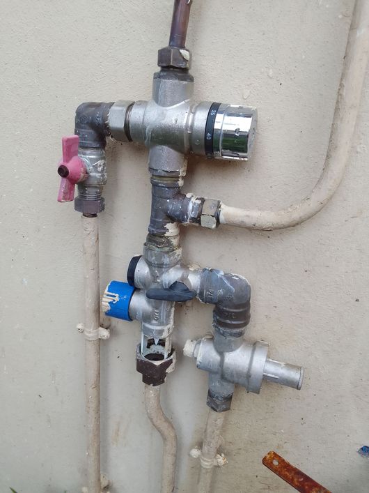 Tuyaux de plomberie muraux avec robinets d'arrêt et raccords rouges et bleus sur un mur beige.