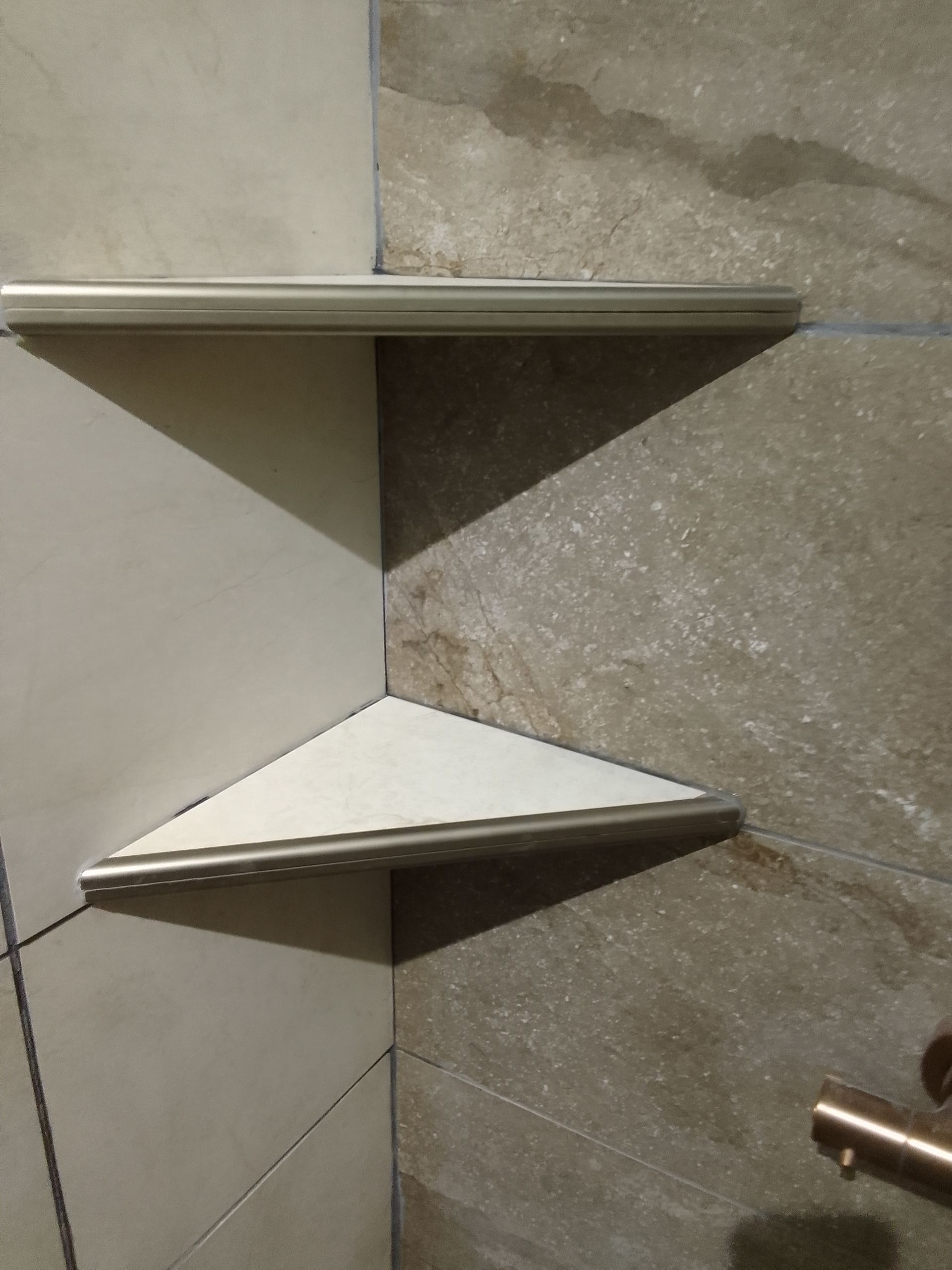 Étagères d'angle fixées sur les murs carrelés d'une douche.