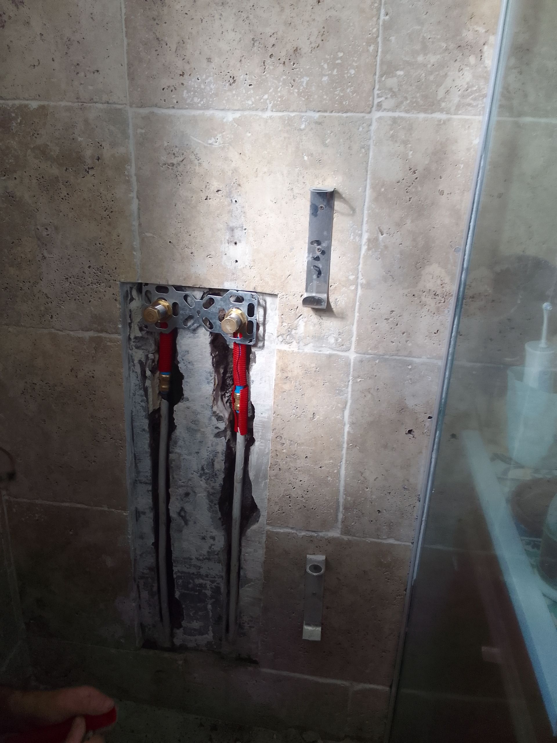 Mur de douche partiellement carrelé avec tuyauterie apparente et paroi de douche en verre sur la droite