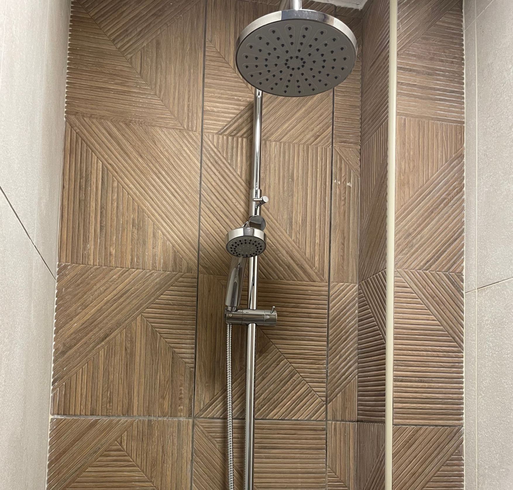 Douche moderne avec pommeau de douche effet pluie et douchette chromée sur carrelage imitation bois.