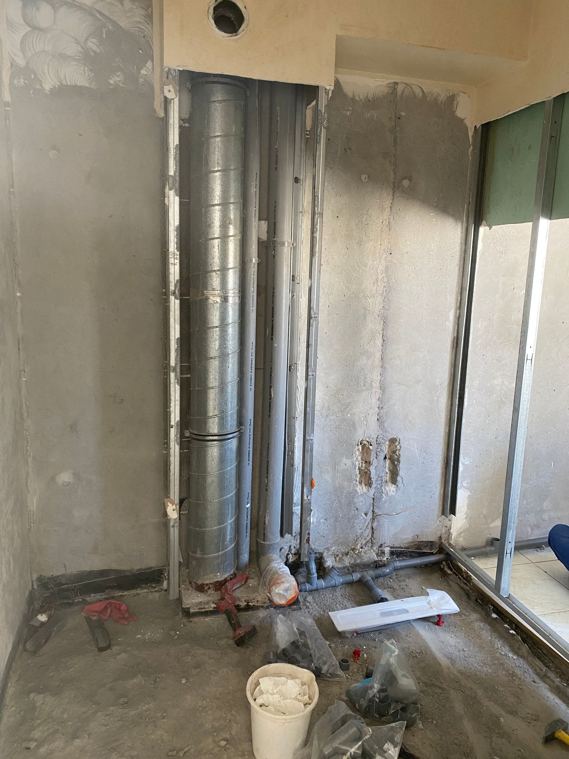 Pièce inachevée avec conduits d'aération apparents, cloisons sèches nues, débris au sol et un seau au premier plan.