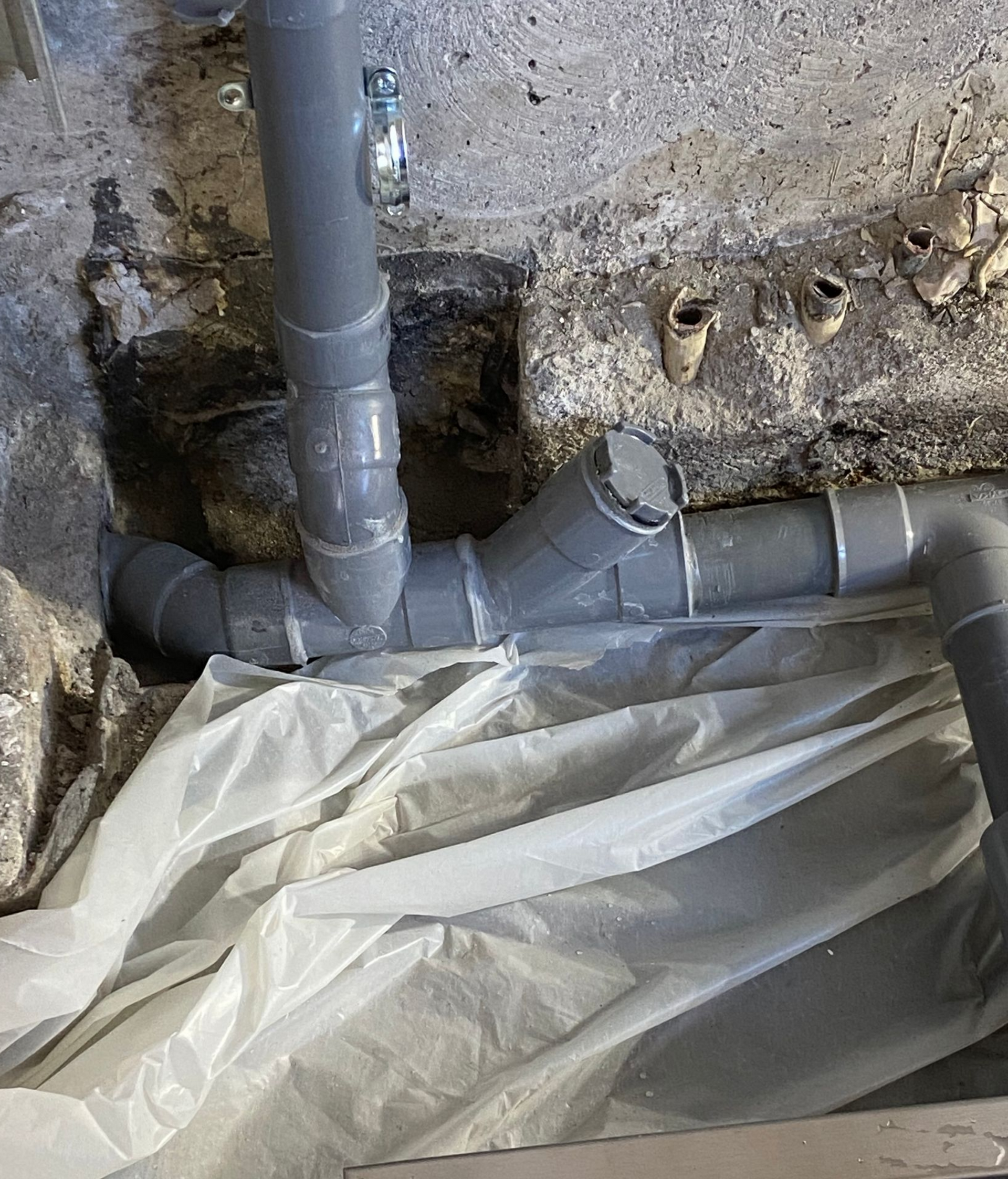 Des tuyaux en PVC gris, raccordés dans une ouverture dans un mur en béton brut, sont partiellement recouverts d'une bâche en plastique.
