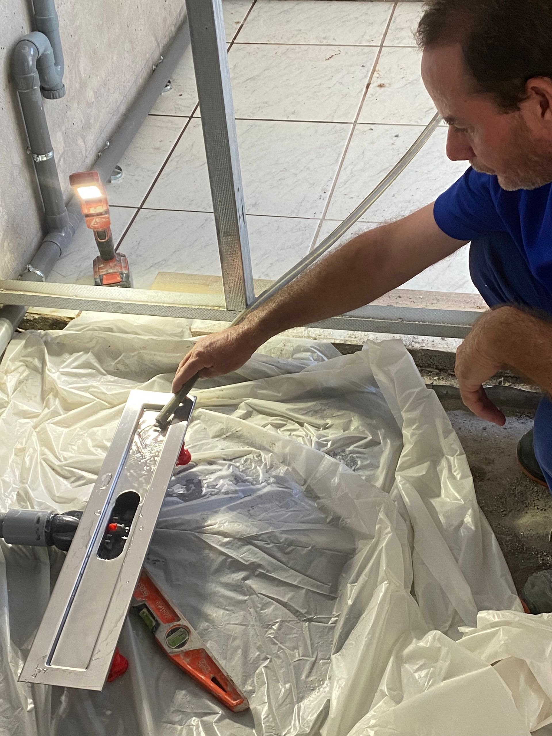Un homme utilise un niveau pour mesurer une surface au sol recouverte d'une bâche en plastique.