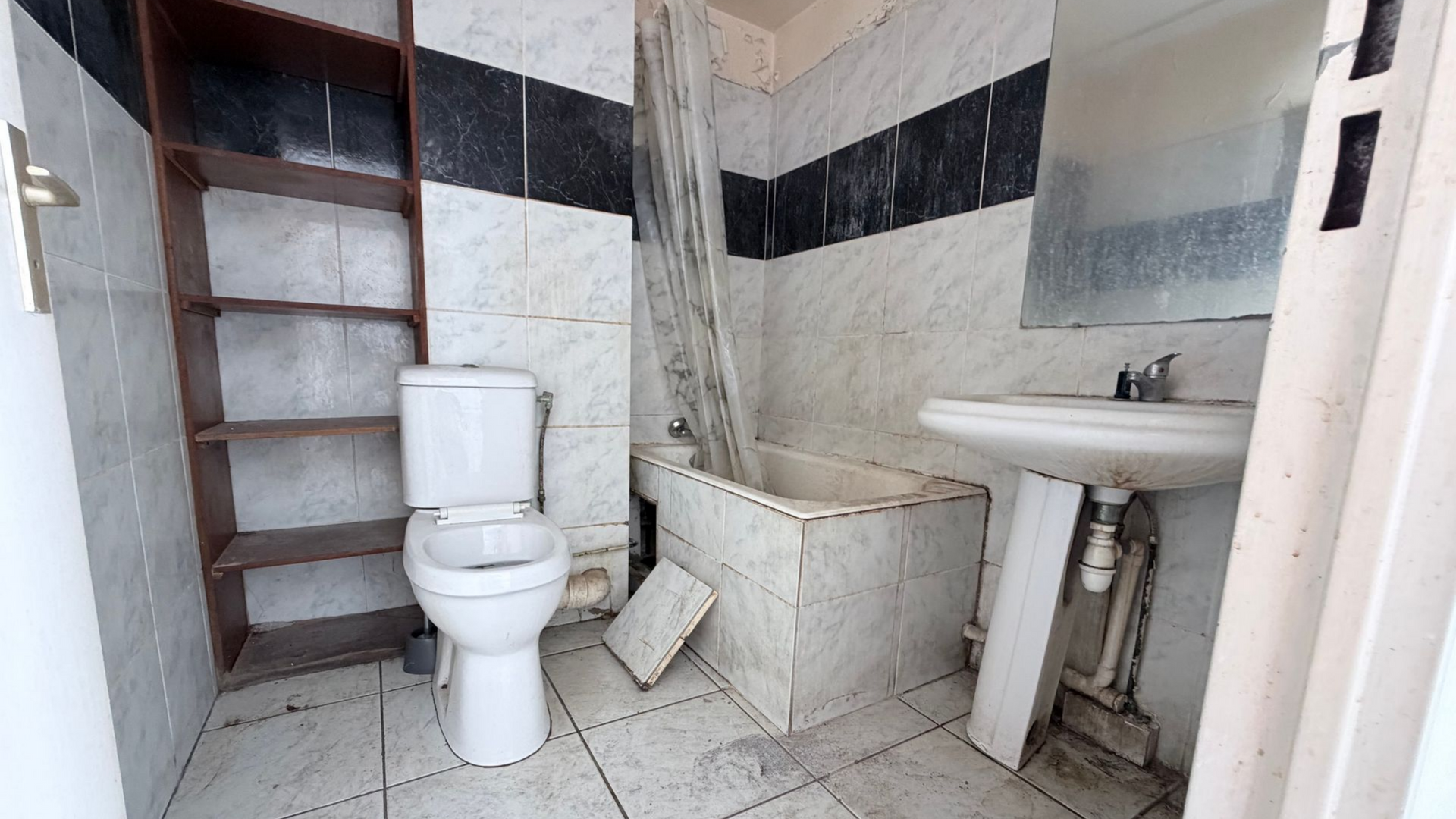 Petite salle de bains très abîmée, carrelée, avec toilettes, lavabo et baignoire.