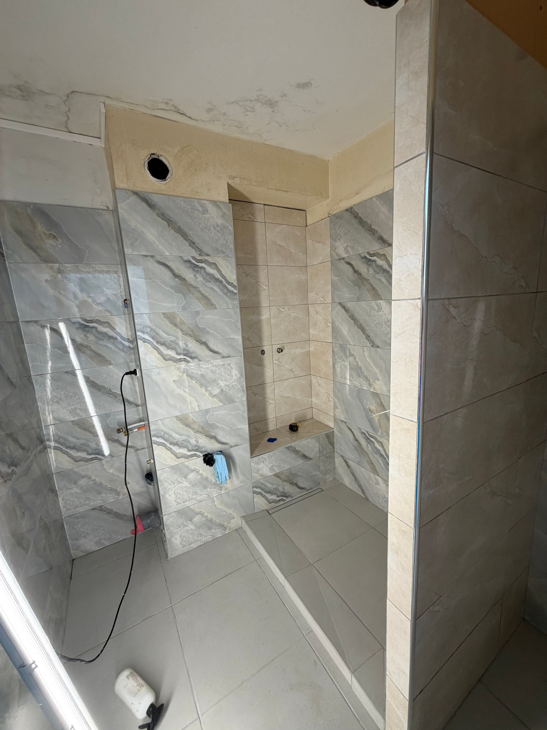 Douche carrelée en cours de construction avec murs imitation marbre, niche encastrée et ouvertures pour la plomberie.