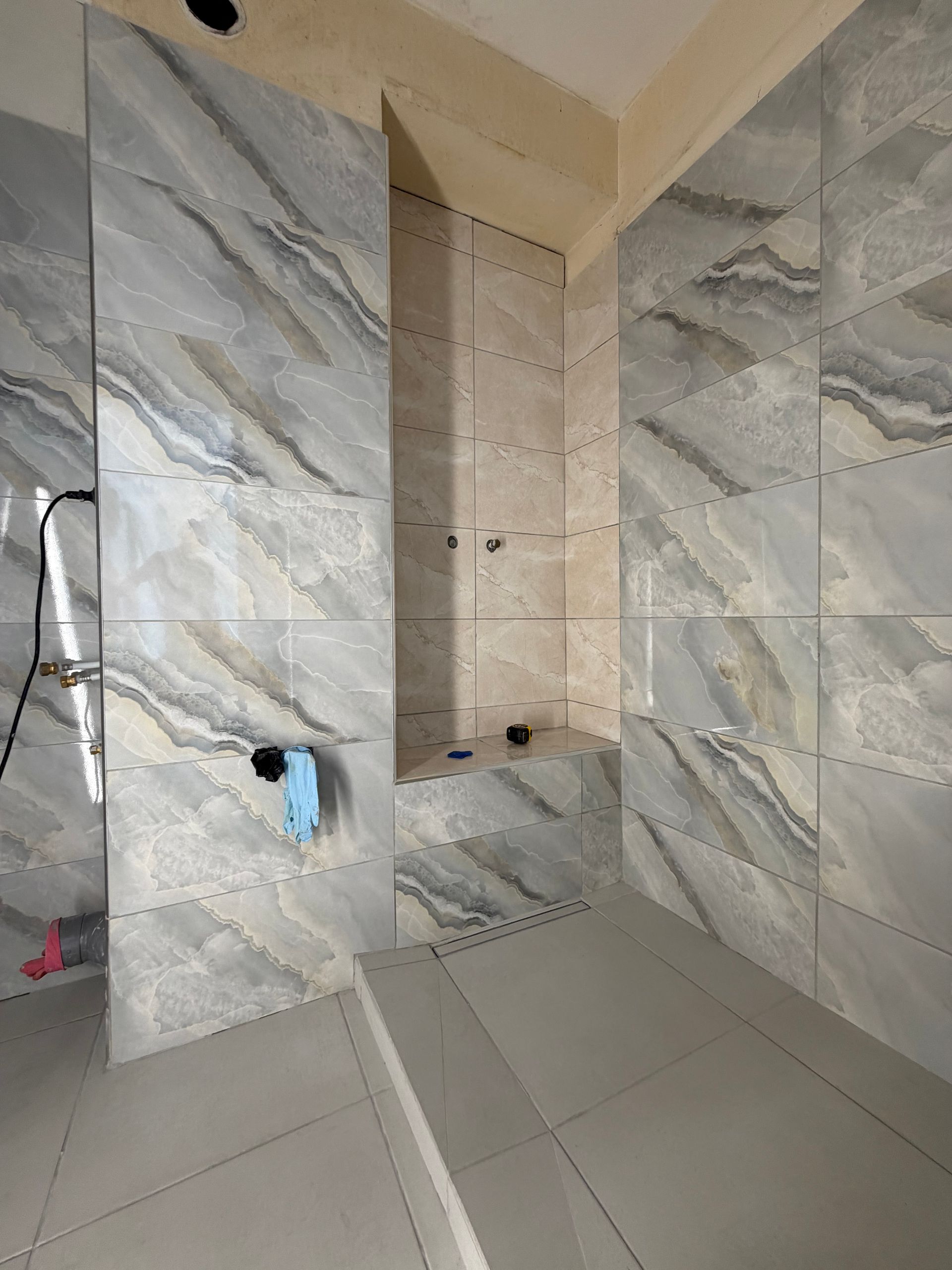 Douche carrelée avec des carreaux muraux en marbre et une niche murale en cours de travaux.