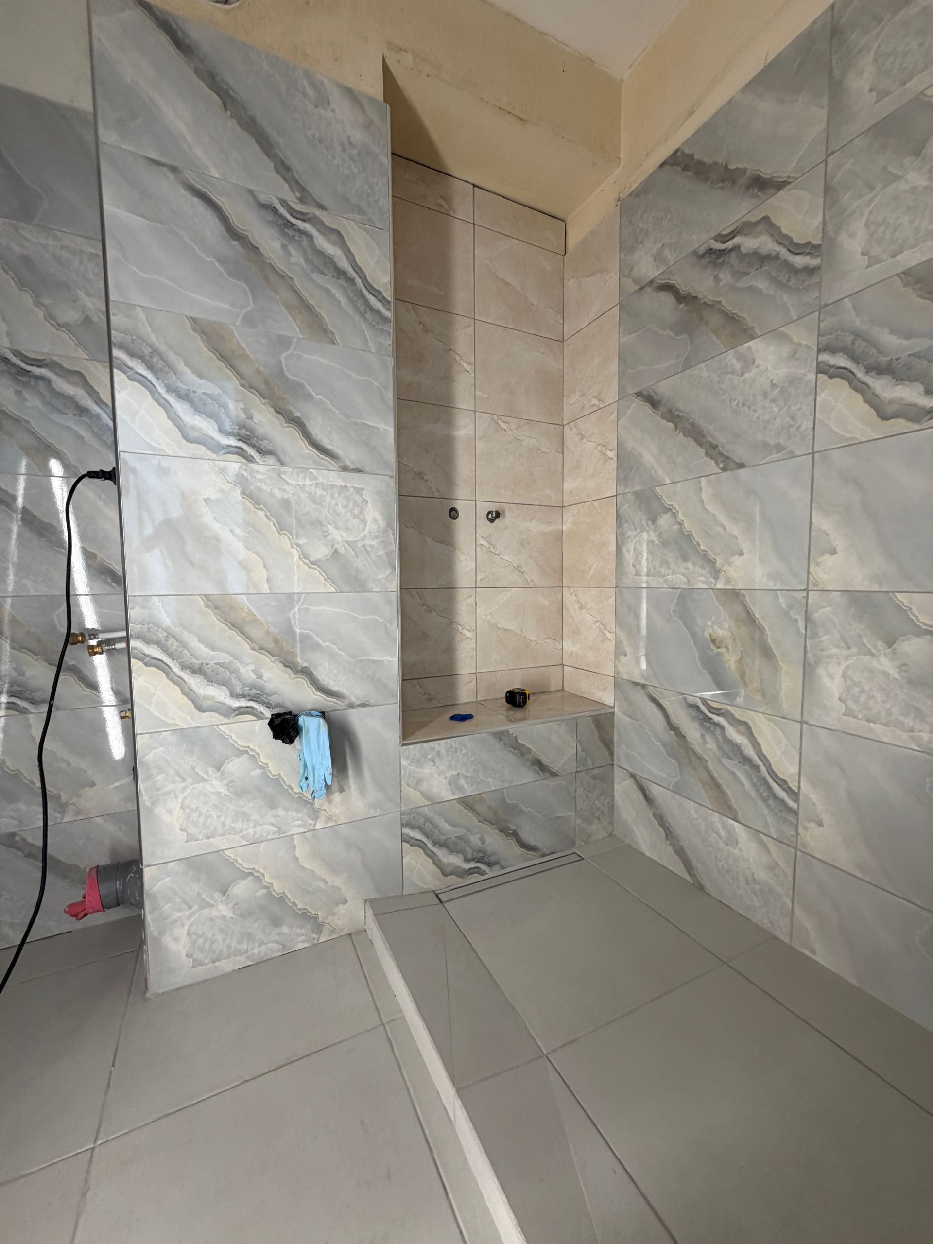 Cabine de douche carrelée avec murs imitation marbre, niche intégrée et robinetterie apparente, en cours de rénovation.