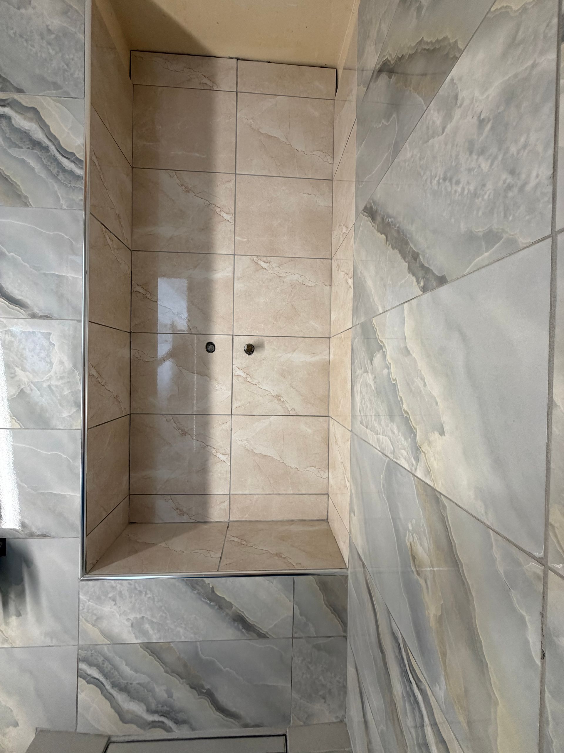 Cabine de douche carrelée, avec des carreaux imitation marbre t une niche murale intégrée.