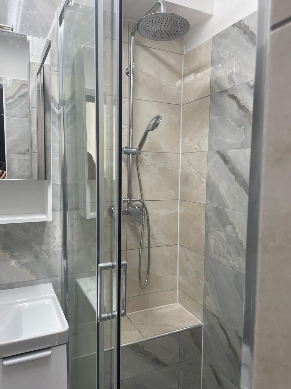 Cabine de douche moderne carrelée avec porte en verre, douche de tête et douchette à main.