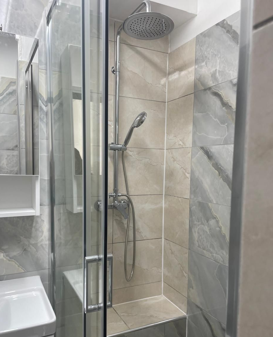 Douche à l'italienne avec porte en verre, pommeau de douche chromé et murs carrelés beiges.