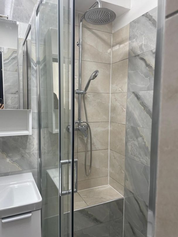 Cabine de douche moderne avec porte en verre, murs carrelés et douchette à main.