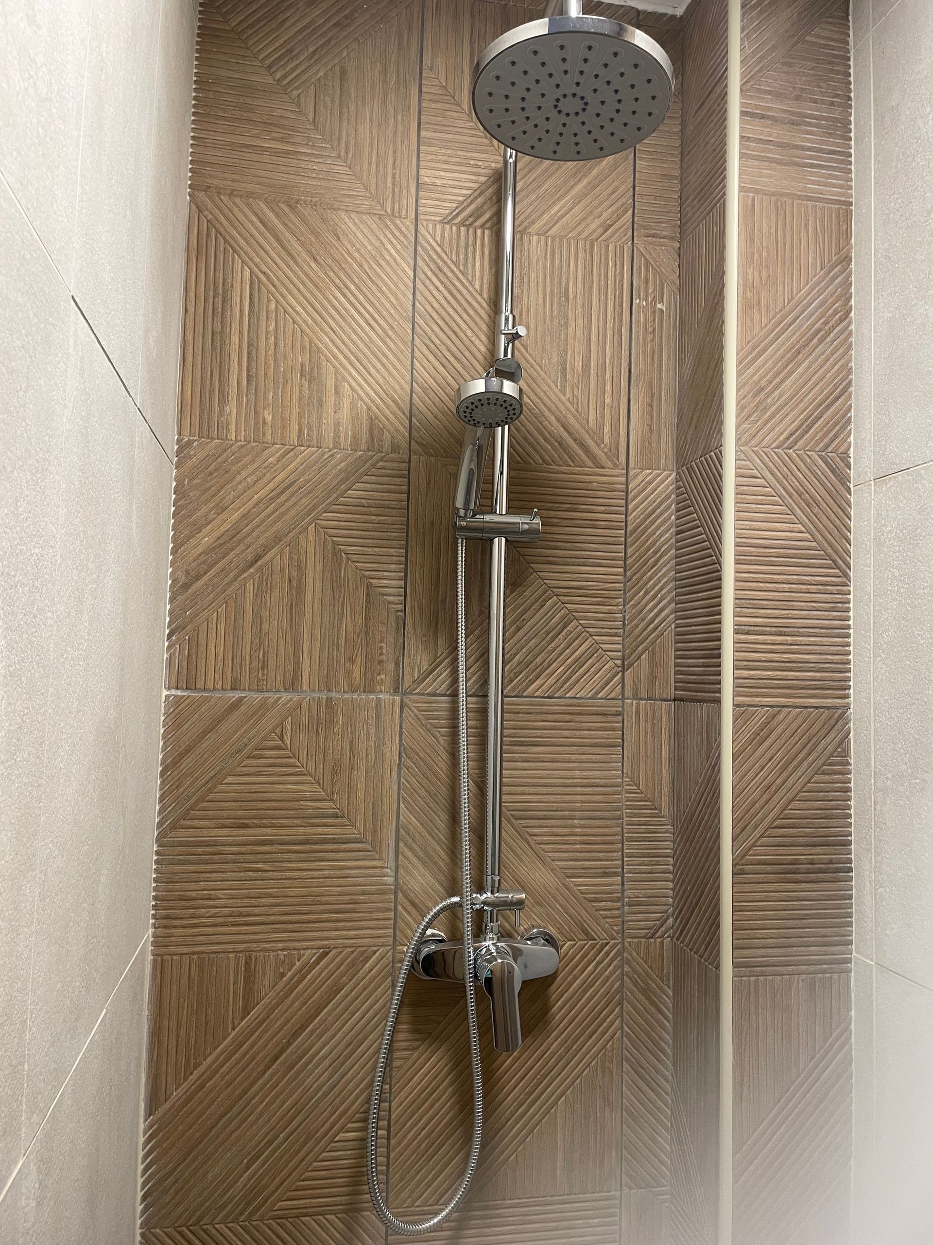 Cabine de douche avec pommeau de douche chromé, flexible et revêtement imitation bois.
