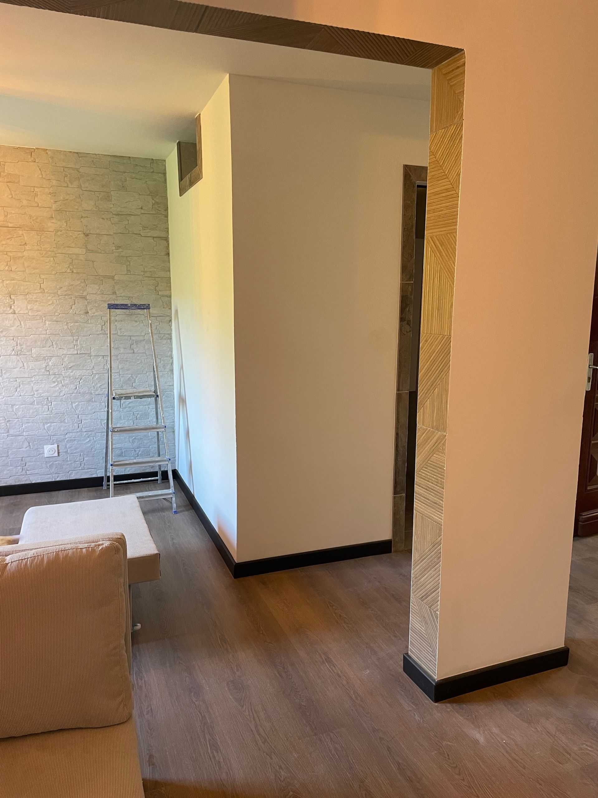 Salon moderne avec parquet, mur en pierre et échelle près d'une porte ouverte.