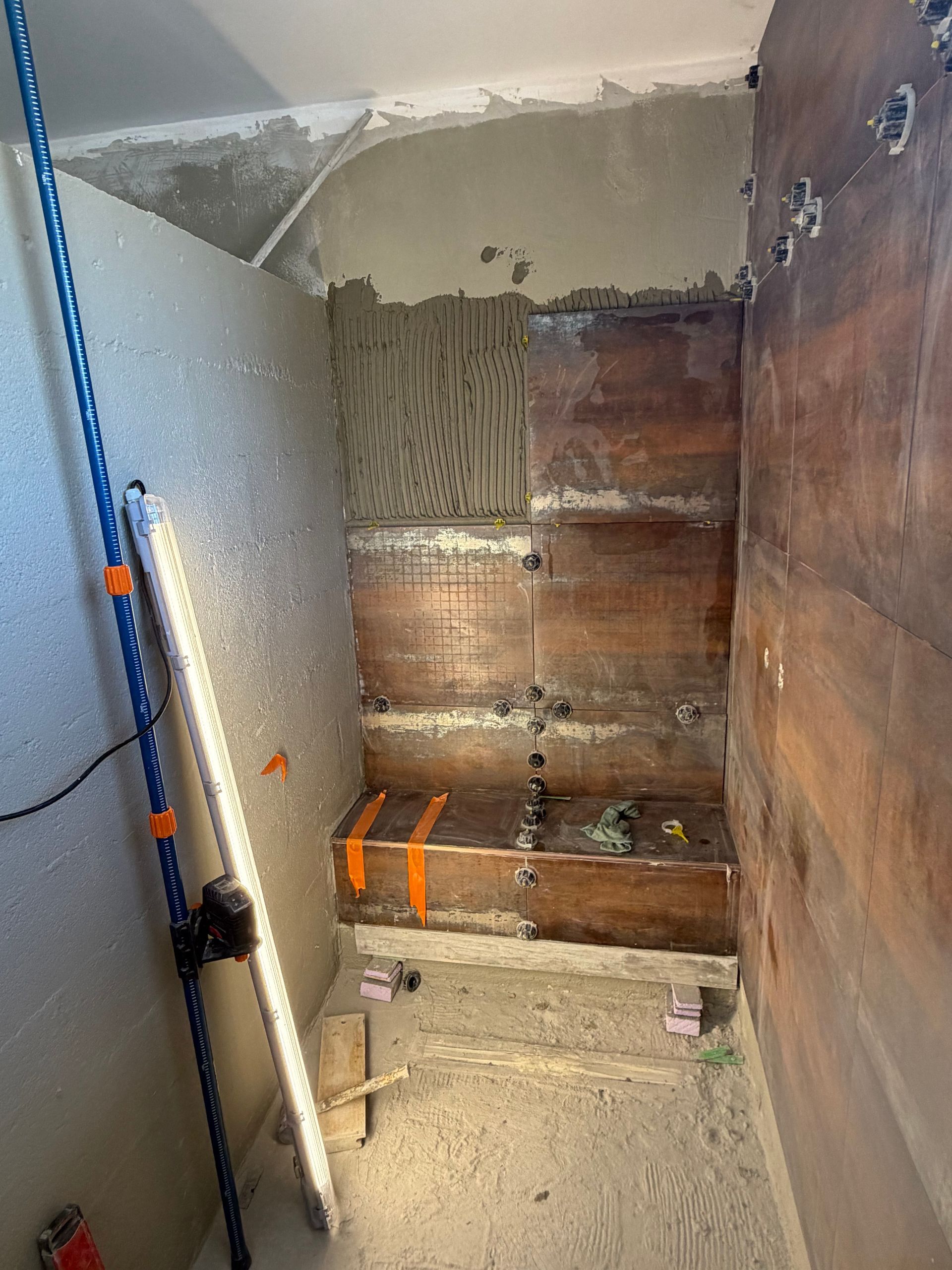 Mur de salle de bains partiellement carrelé avec enduits et raccords de robinnetterie apparents.
