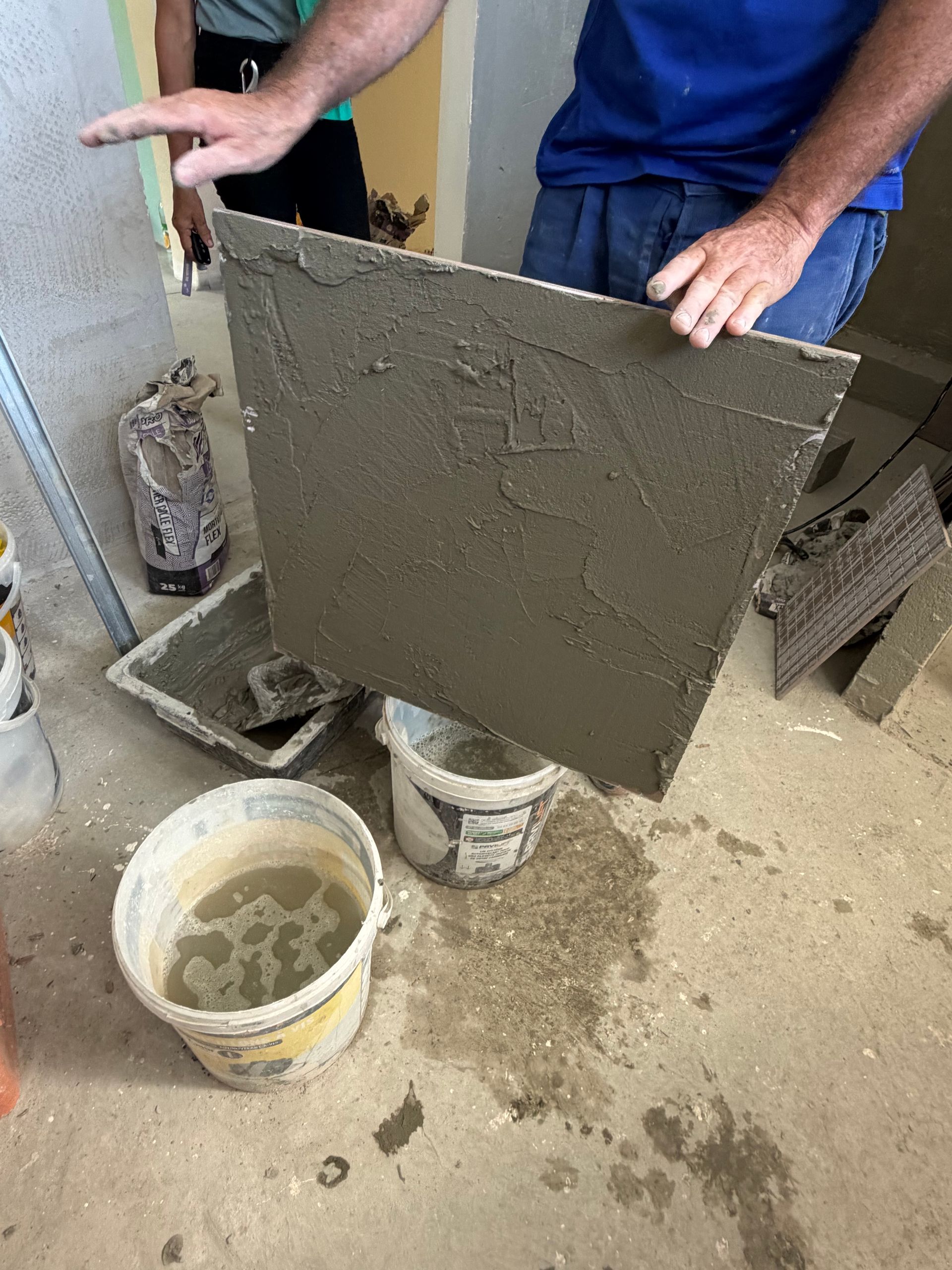 Des ouvriers lissent du béton frais sur un grand carreau de carrelage, à l'aide de seaux et d'outils.