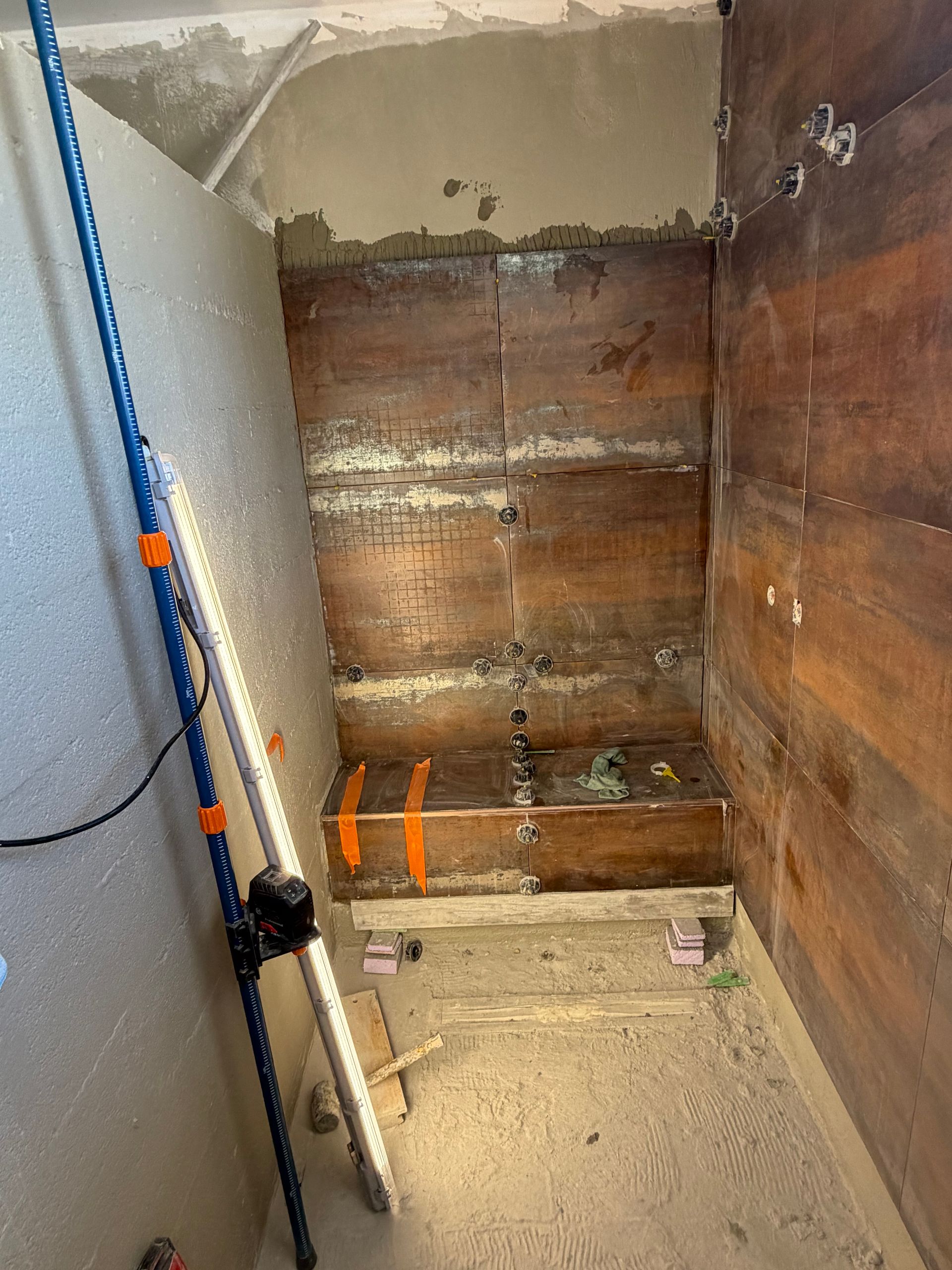 Une cabine de douche en rénovation, avec enduits apparents et mur carrelé marron.