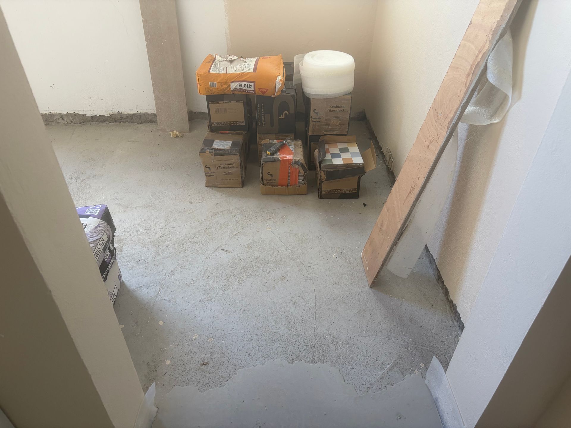 Pièce partiellement rénovée avec des outils et des récipients empilés contre le mur du fond.