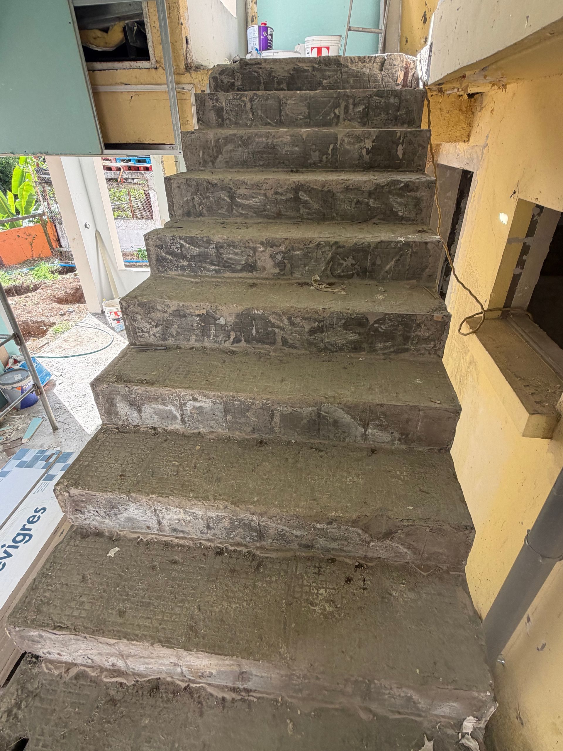 Escalier étroit en béton en construction à l'intérieur d'un bâtiment, avec des murs inachevés et des débris à proximité.