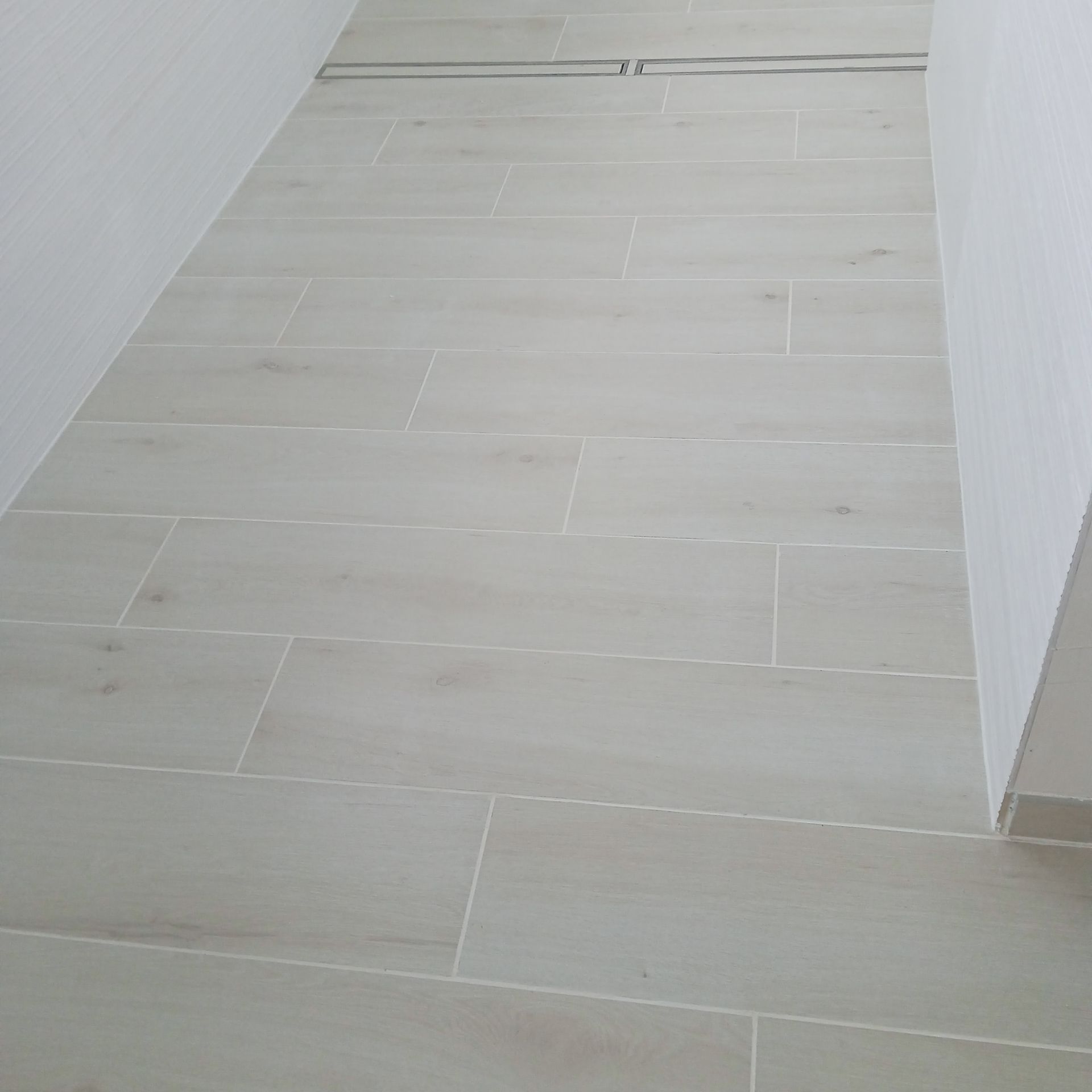 Couloir étroit blanc avec sol carrelé beige clair et murs unis.