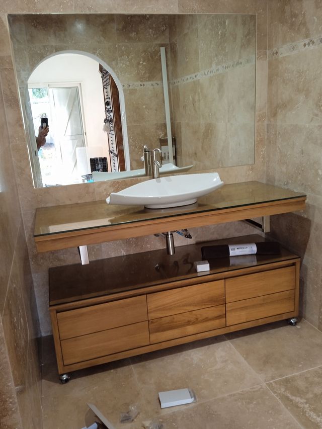 Vasque blanche en céramique, grand miroir et meuble de rangement en bois dans une salle de bains carrelée.