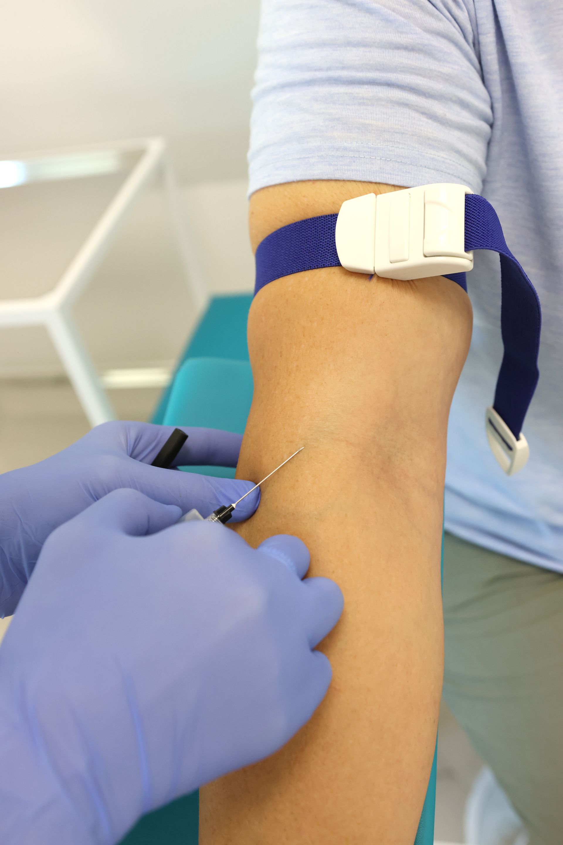 Le bras d'une personne avec un garrot, recevant une injection avec une aiguille par des mains gantées, dans un contexte clinique.