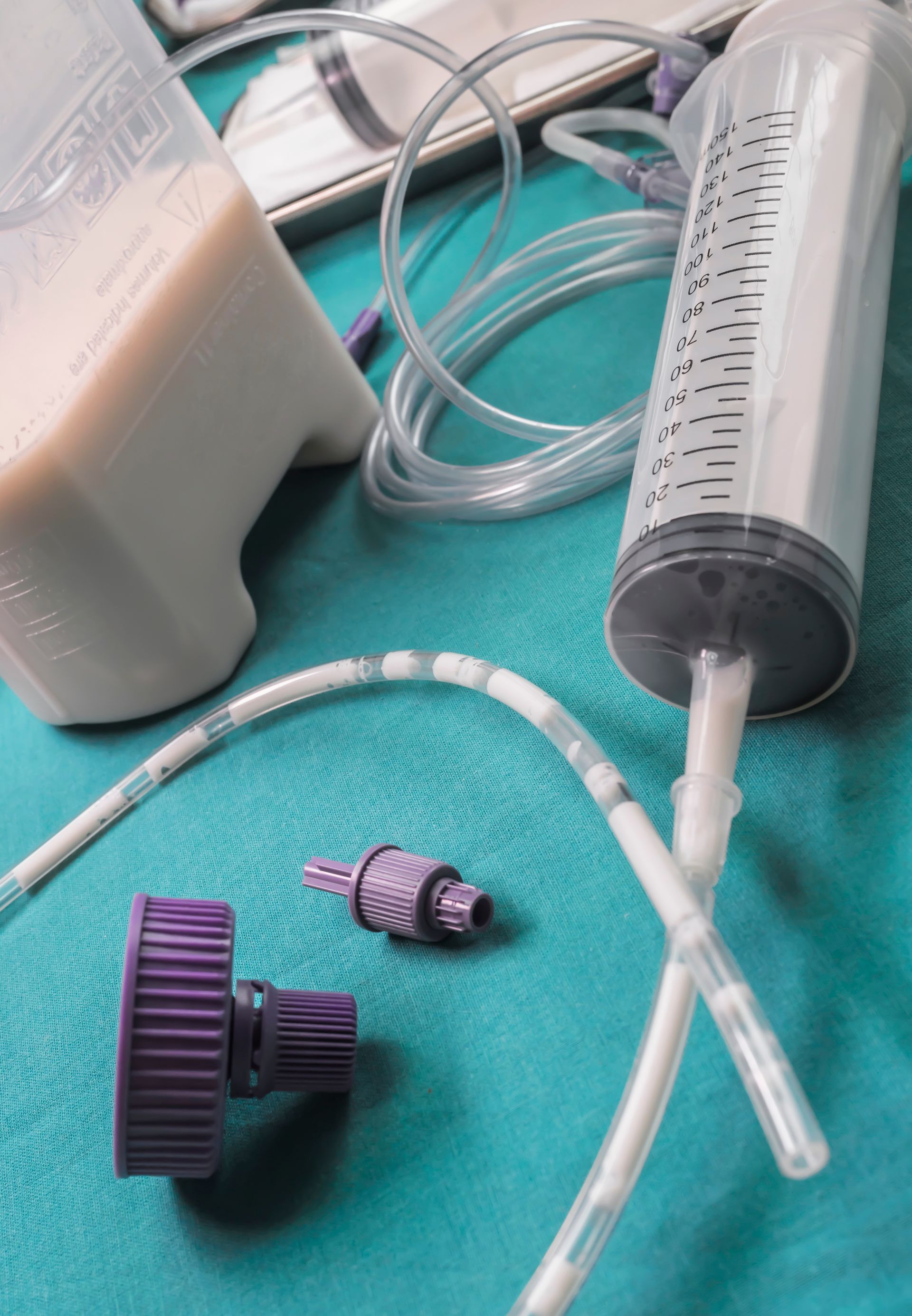 Matériel médical pour l'alimentation par sonde sur une surface verte : poche de liquide, seringue, tubulure et connecteurs.