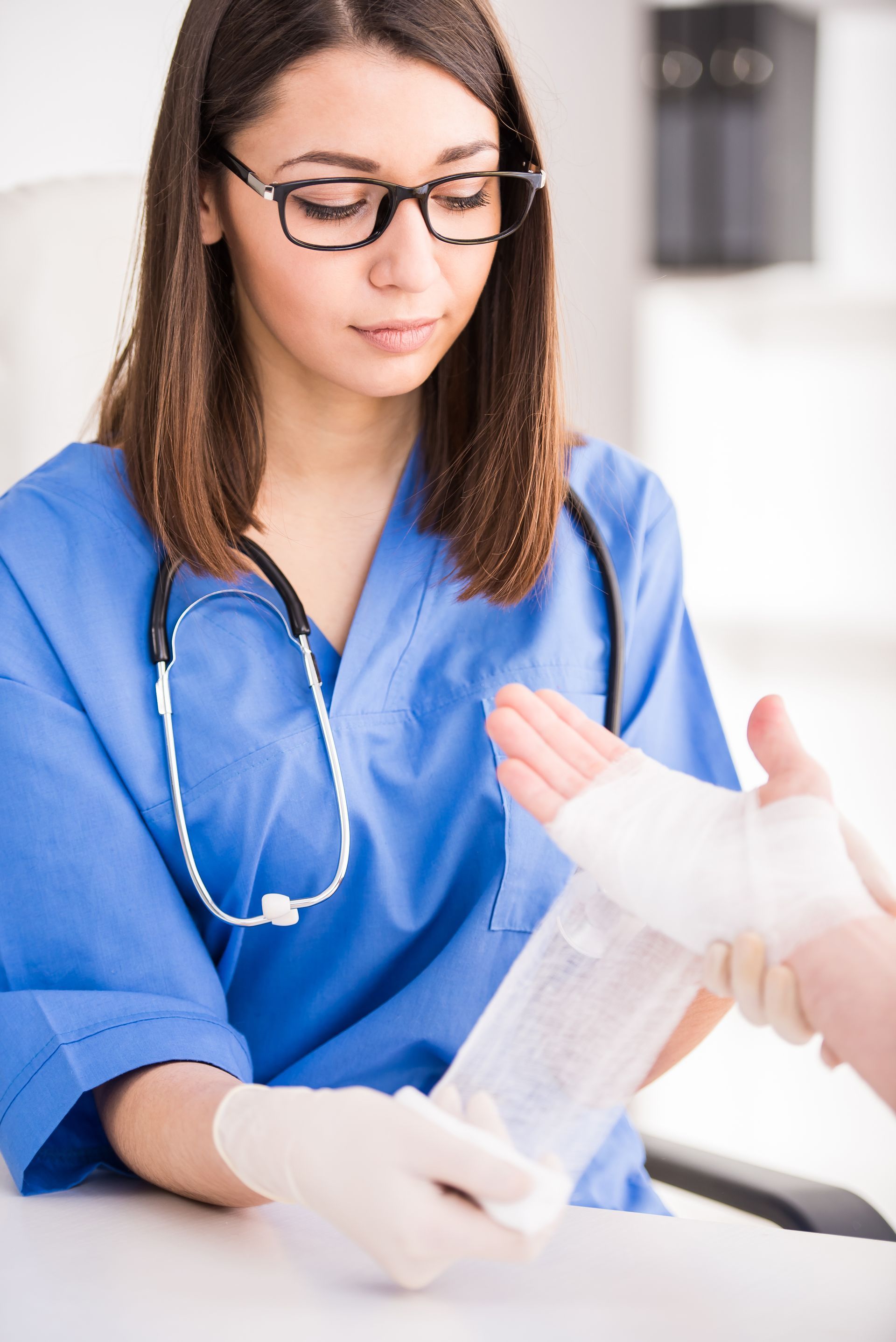 Un médecin en blouse bleue applique un bandage sur la main d'un patient.