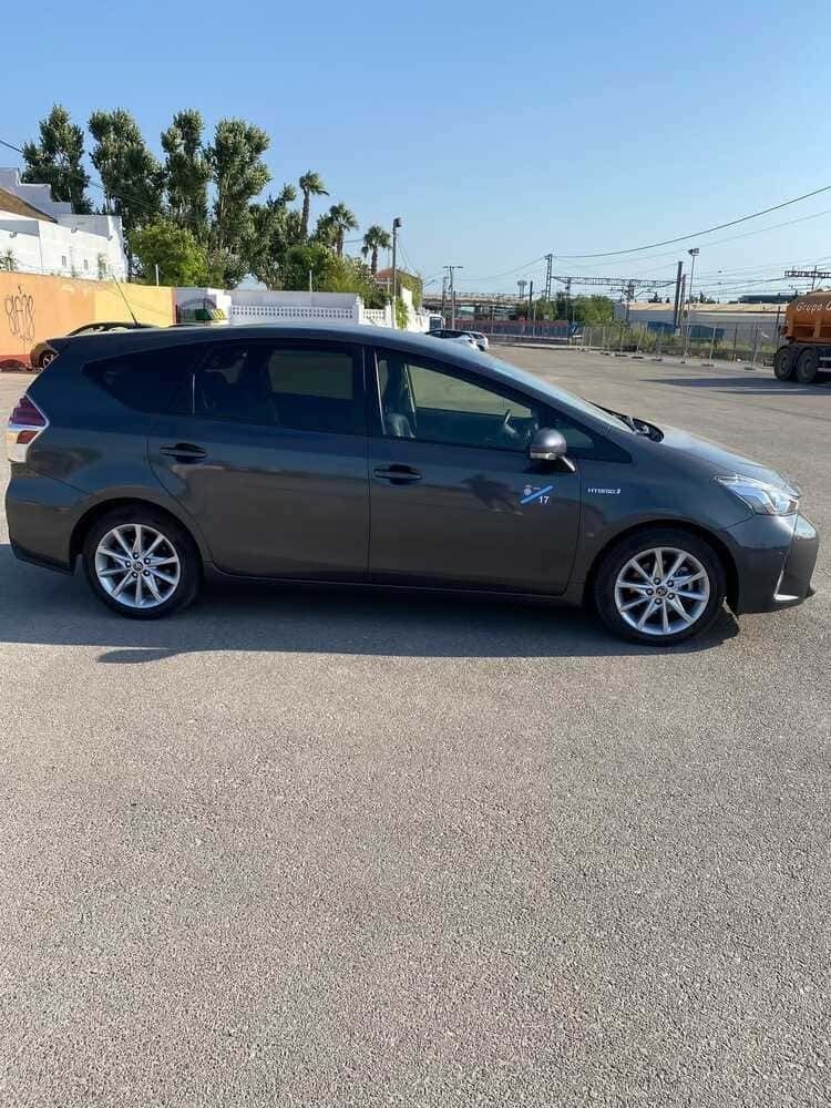 Toyota Prius V gris estacionado sobre asfalto en un estacionamiento soleado al aire libre.