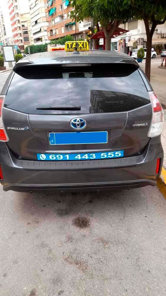 Vista trasera de un taxi Toyota Prius gris oscuro con un número de teléfono en el parachoques.