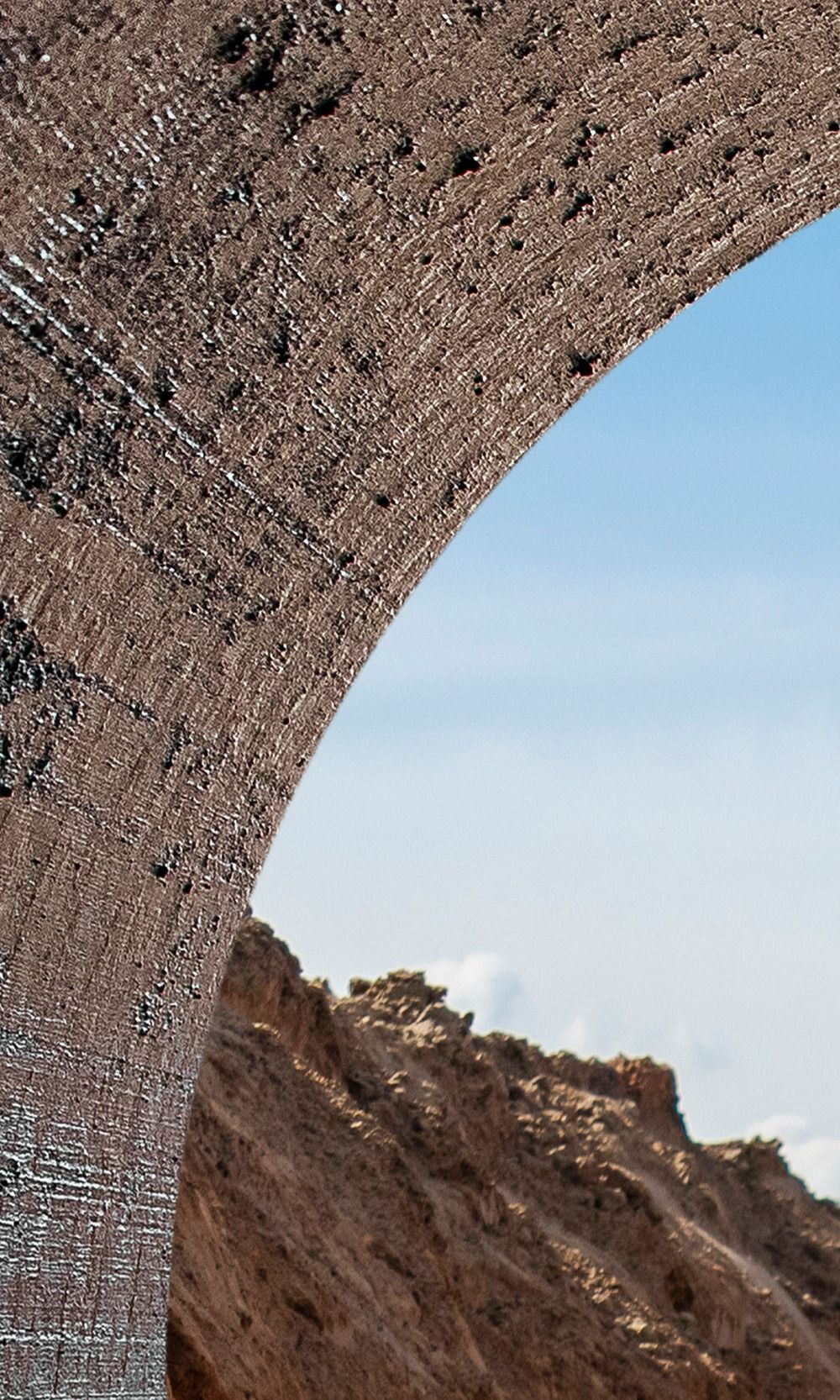 Une arche en pierre encadrant une vue sur un ciel bleu et un paysage rocheux.