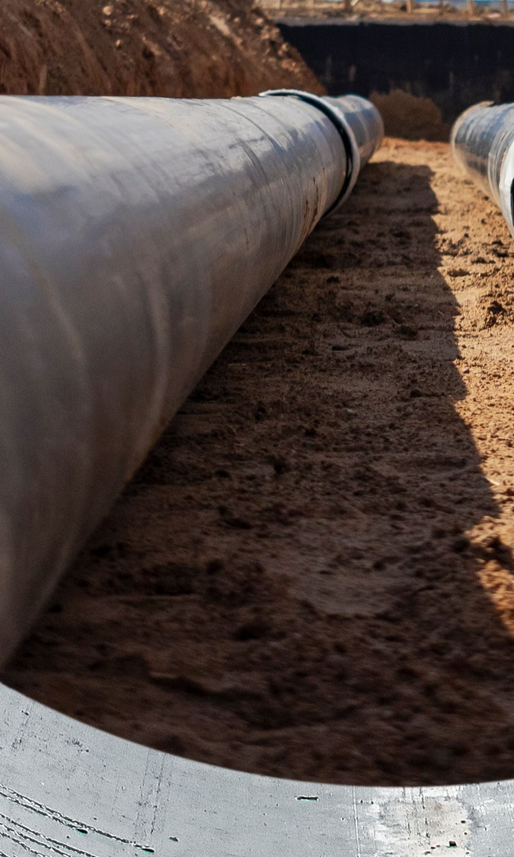 De gros tuyaux ont été posés dans une tranchée de terre brune, probablement pour des infrastructures souterraines.
