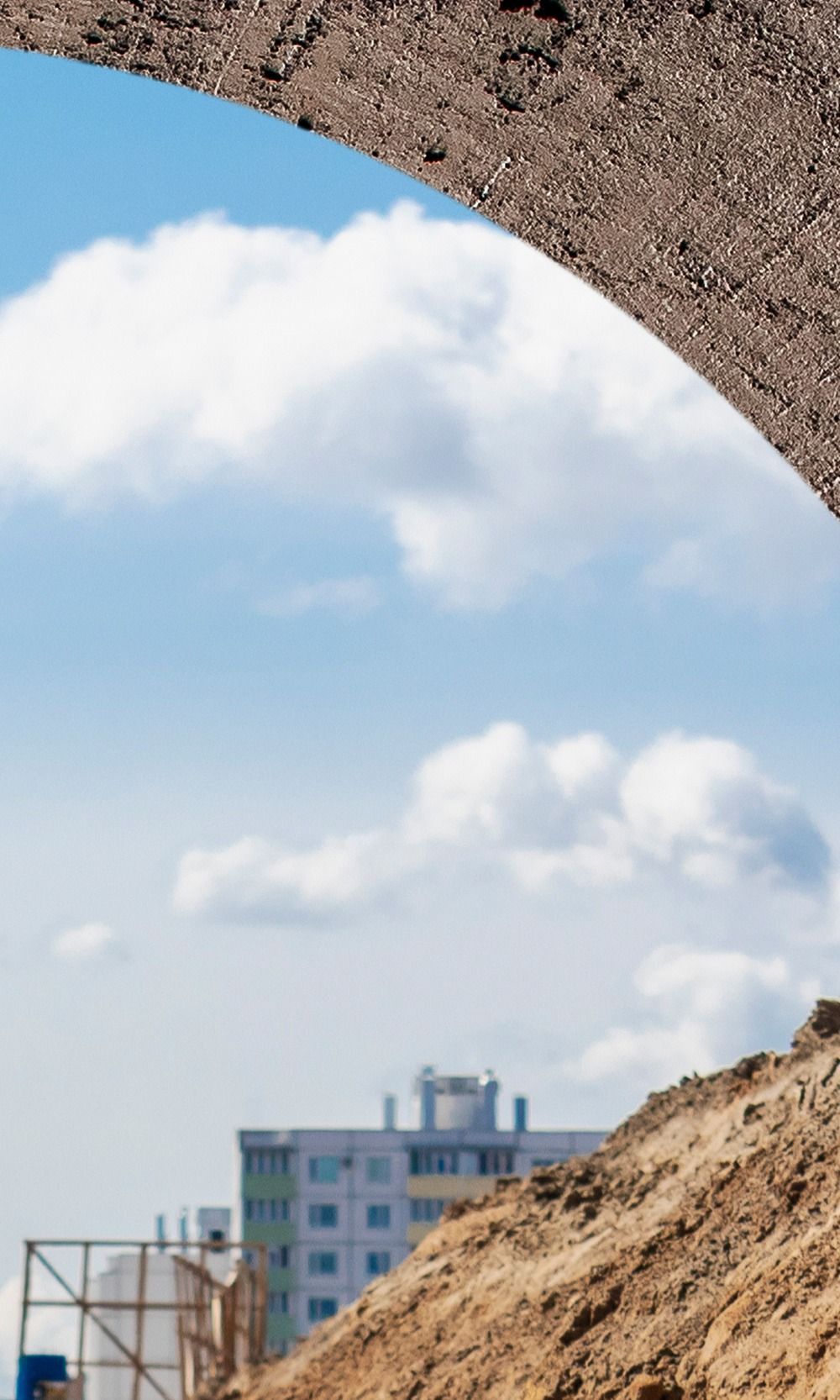 Ciel bleu parsemé de nuages, encadré par un sol à la texture accidentée, avec des bâtiments de la ville en arrière-plan.
