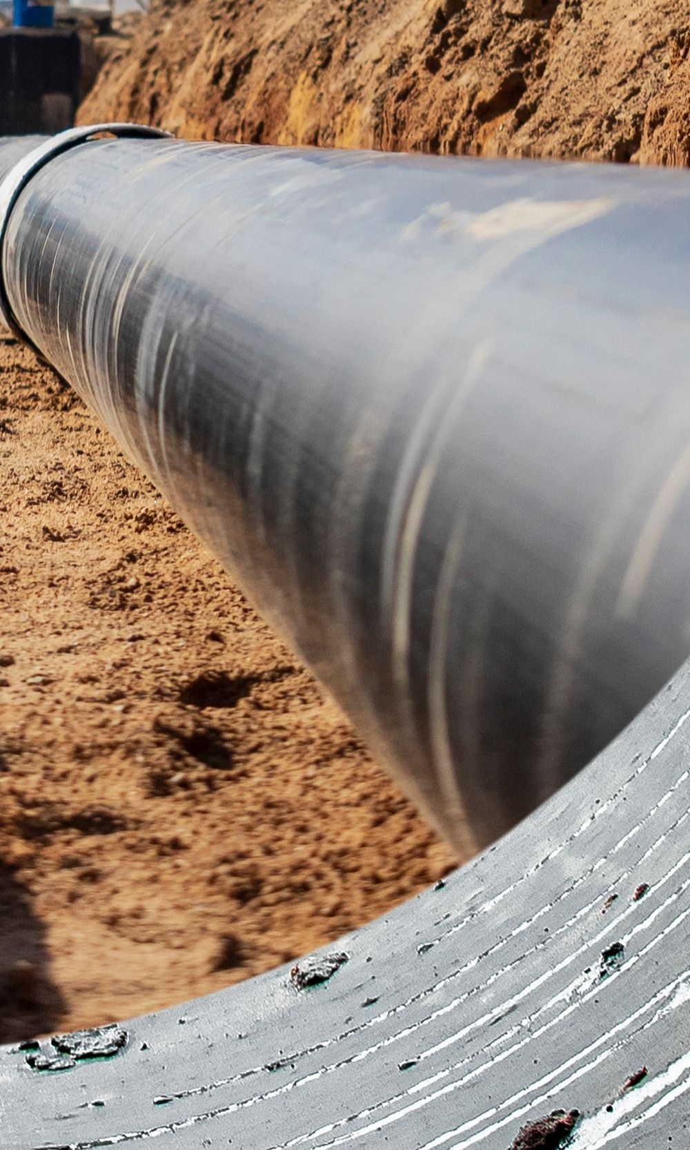 Gros tuyau noir dans une tranchée de terre brune, probablement un élément d'un projet d'infrastructure.