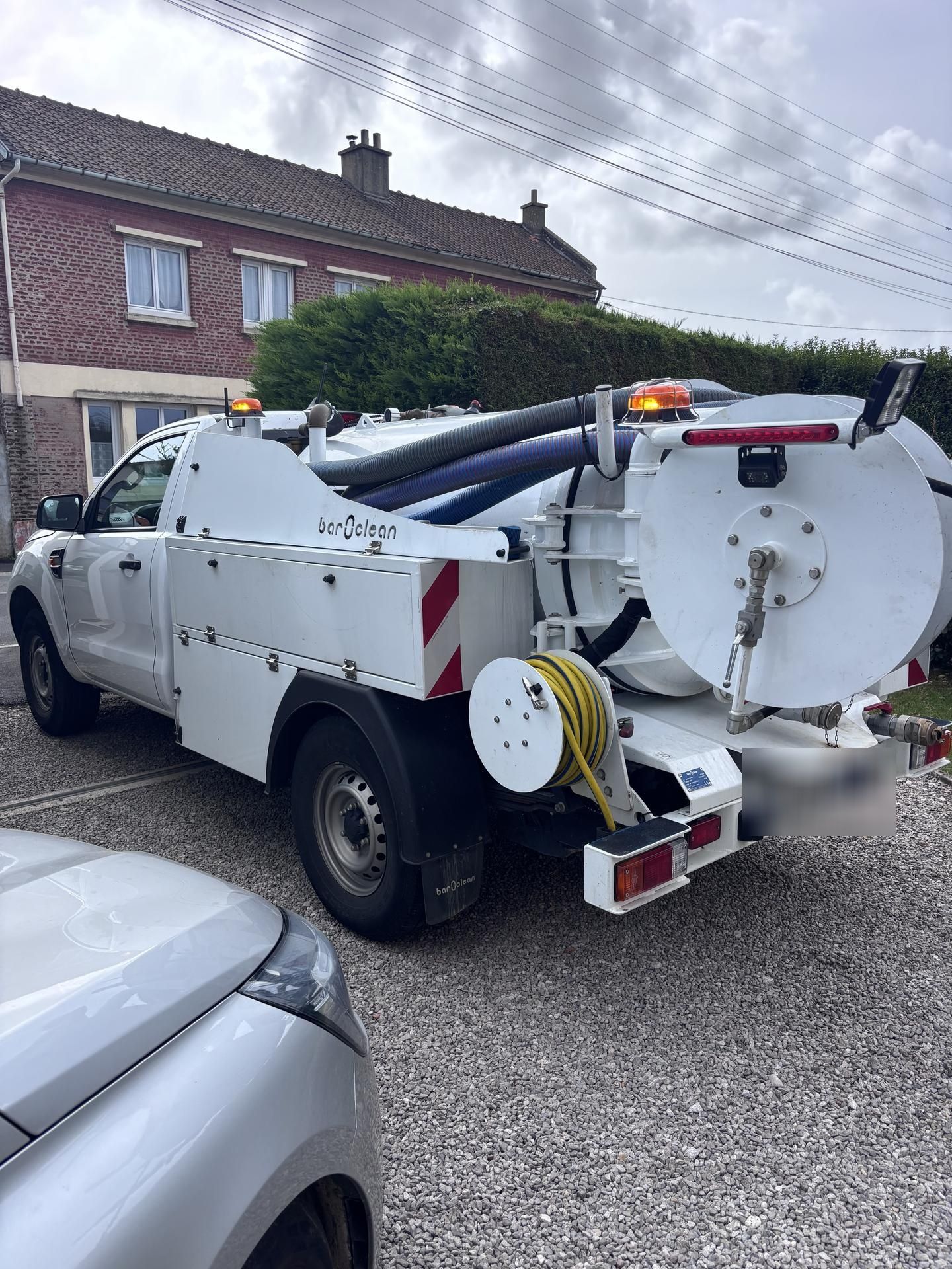 Camion blanc équipé de matériel spécialisé, stationné devant une maison en briques.