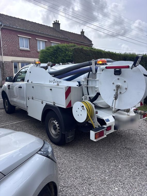 Camion de service blanc avec équipement garé devant une maison en briques.