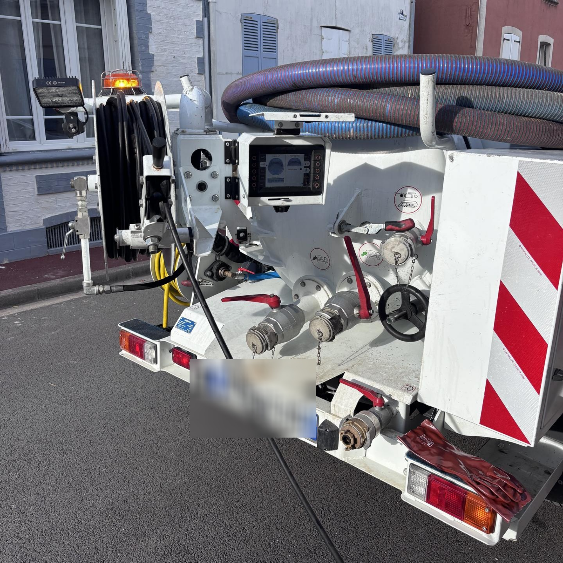 Camion de service blanc et rouge stationné dans une rue ; tuyaux et équipements visibles.