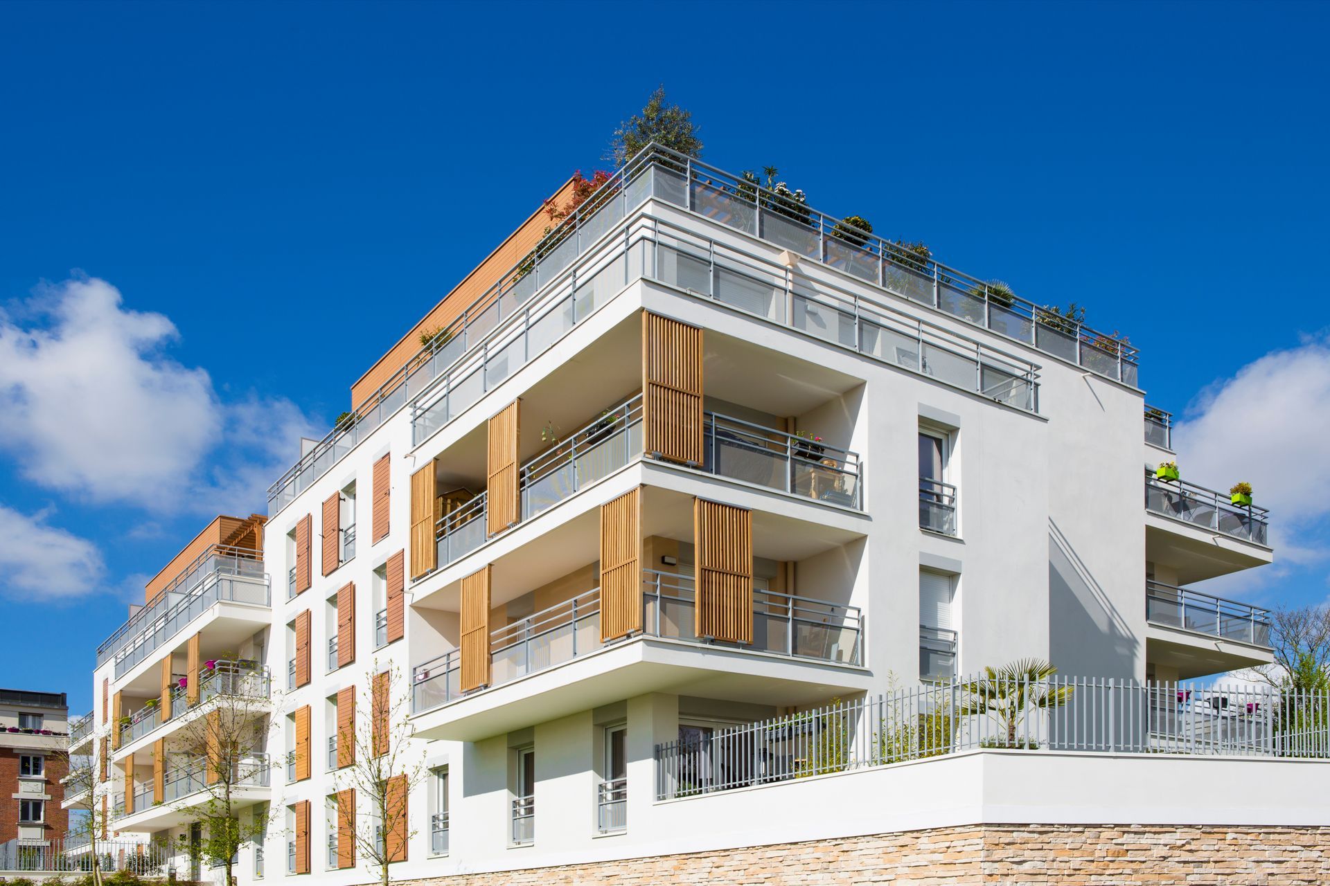 Immeuble d'appartements moderne blanc avec balcons, éléments en bois et terrasse sur le toit se détachant sur un ciel bleu.
