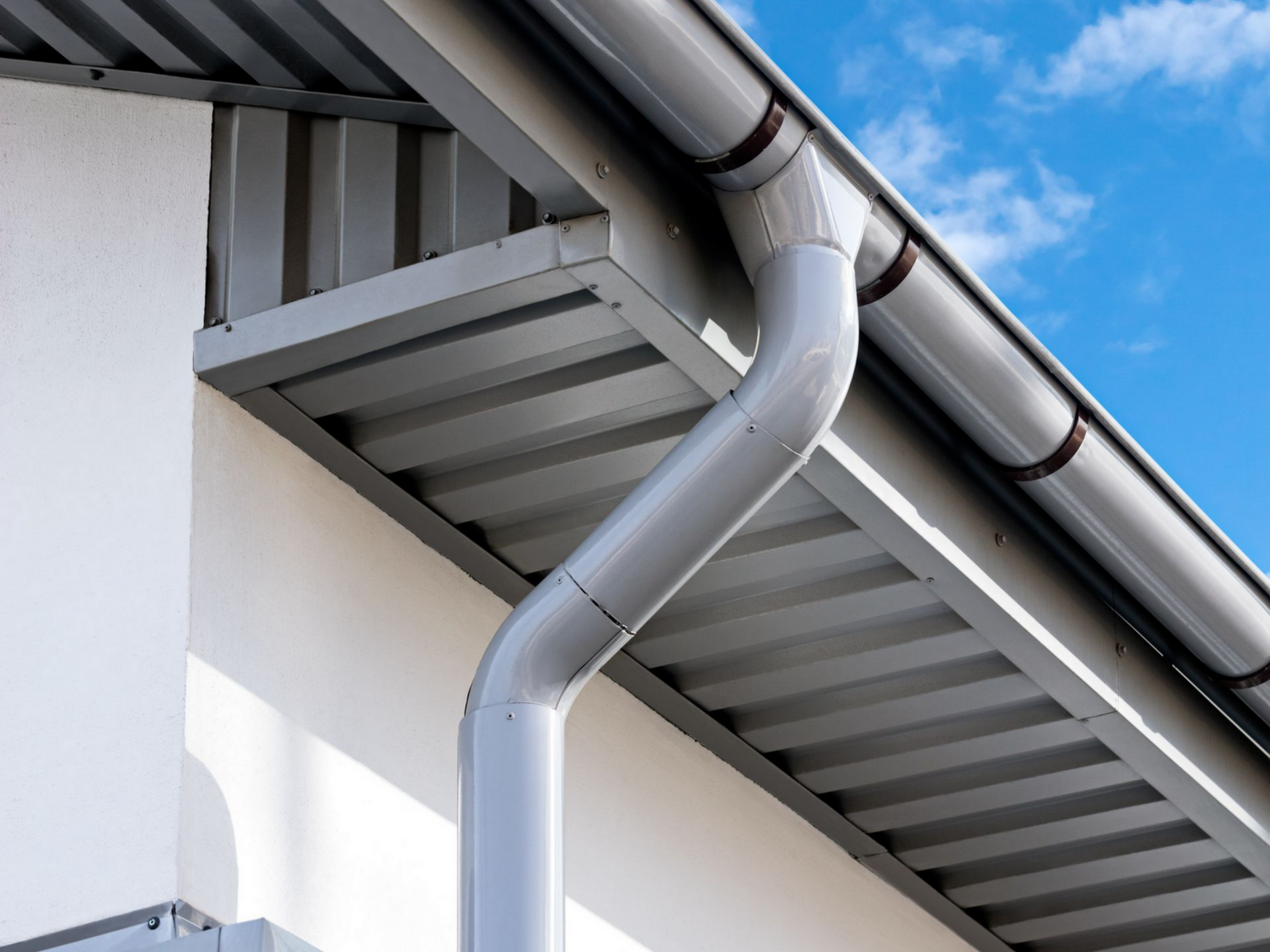 Système de gouttière grise sur un bâtiment blanc, avec un ciel bleu en arrière-plan.