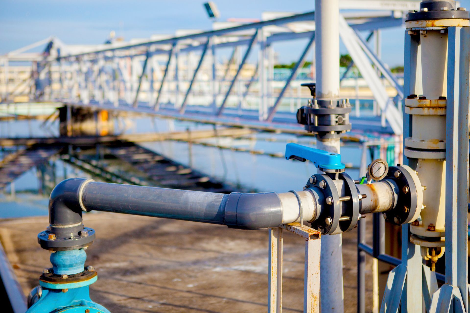 Tuyaux et vannes d'une station d'épuration des eaux, avec une poignée bleue et un pont en arrière-plan.