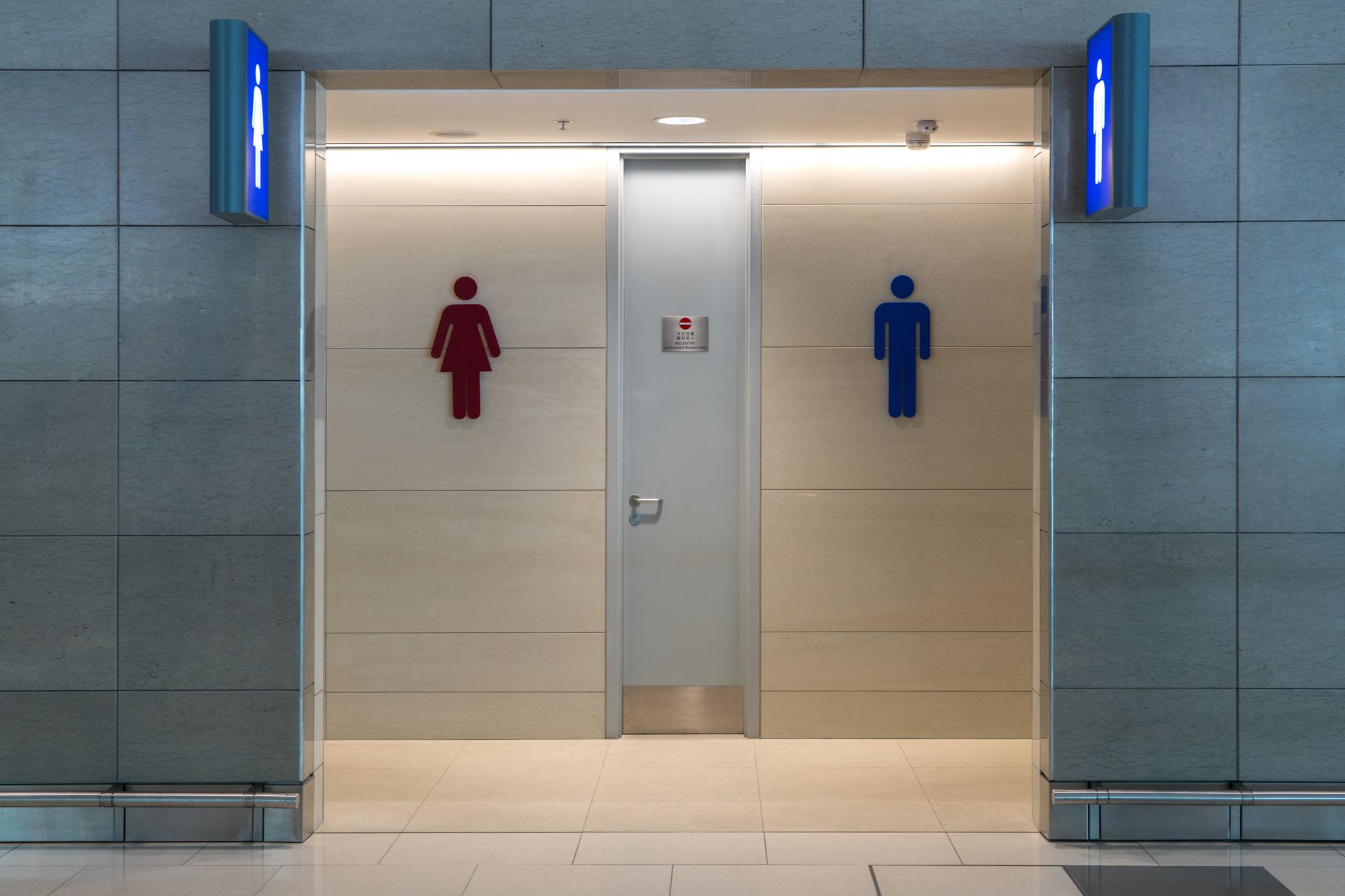 Entrée des toilettes publiques, avec des icônes de genre rouges et bleues au-dessus des portes.