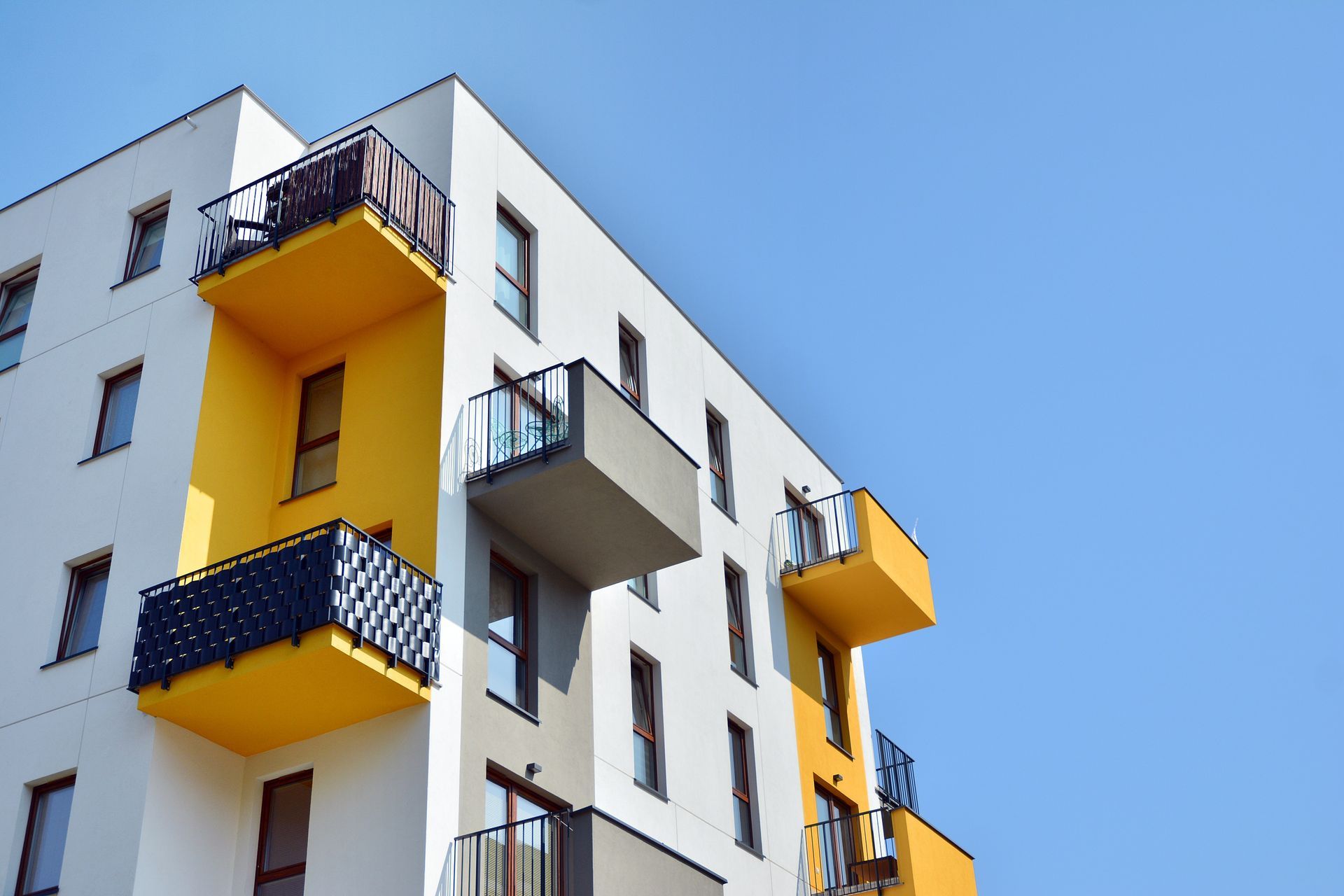 Immeuble d'appartements moderne, blanc et jaune, avec balcons se détachant sur un ciel bleu azur.