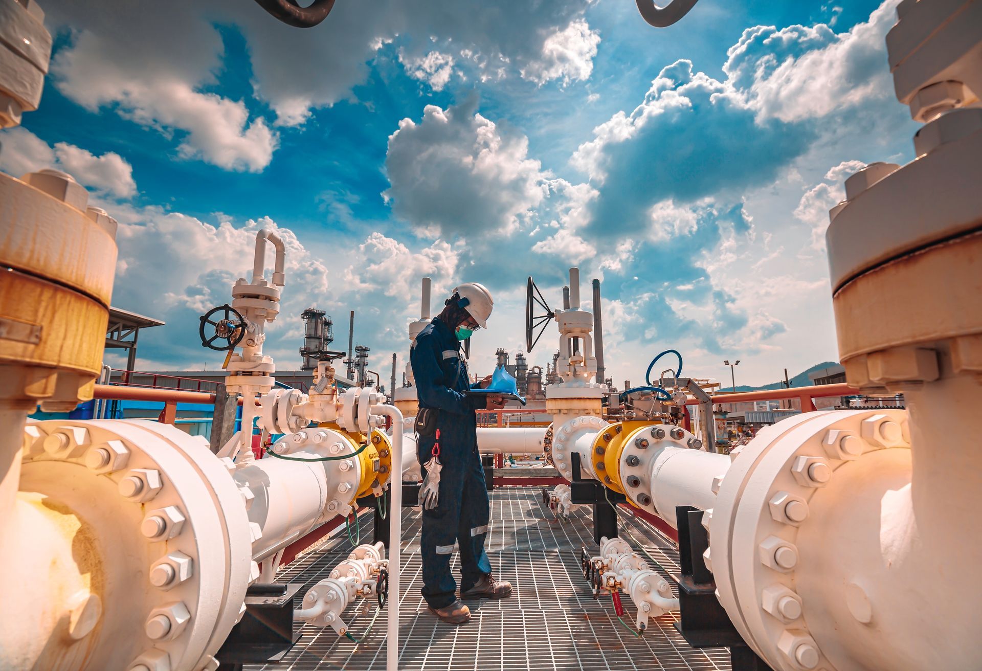 Un technicien inspecte des canalisations dans une usine sous un ciel bleu nuageux.
