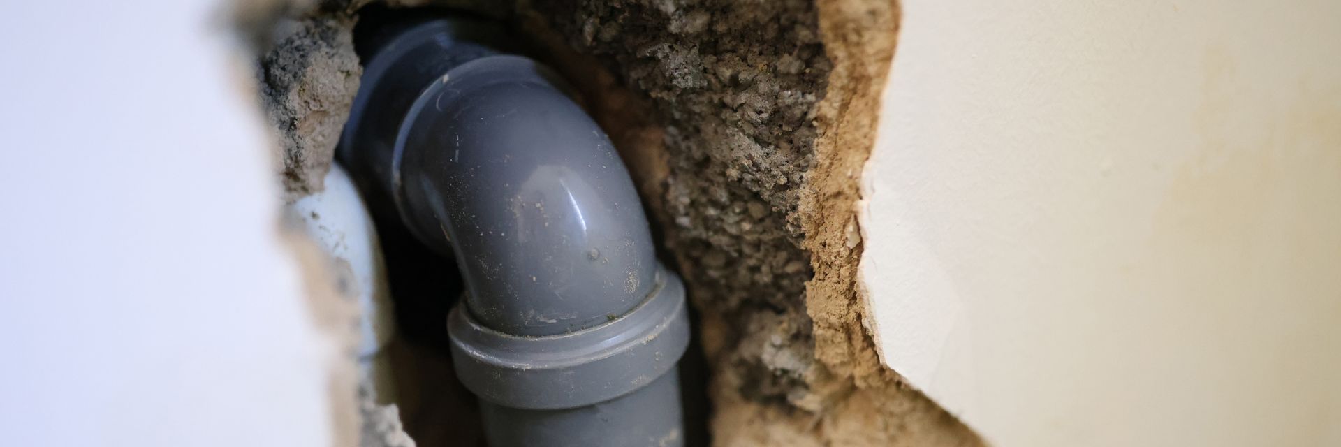 Un coude de tuyau gris sort d'un mur, entouré de moisissures et de matériaux endommagés.