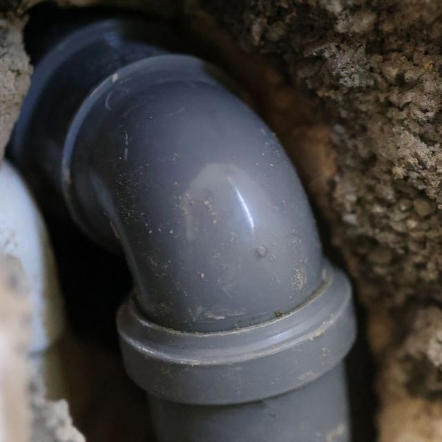 Raccord coudé en PVC gris installé dans un mur rugueux et texturé.