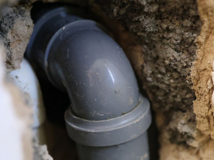Des coudes de tuyau de plomberie en PVC gris se forment à l'intérieur d'un mur en béton brut.