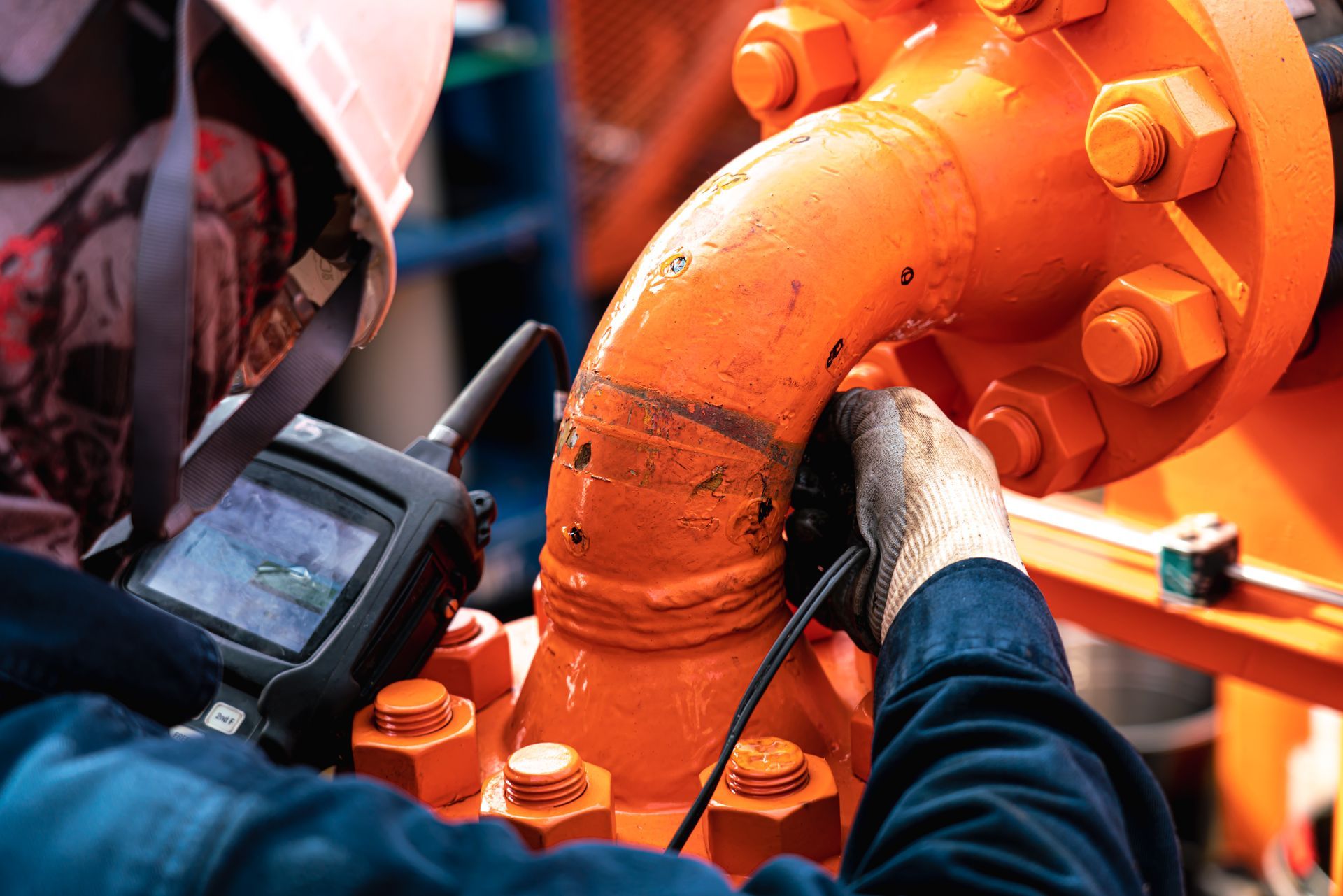 Un inspecteur utilise un appareil portatif pour examiner un tuyau orange muni de gros boulons.